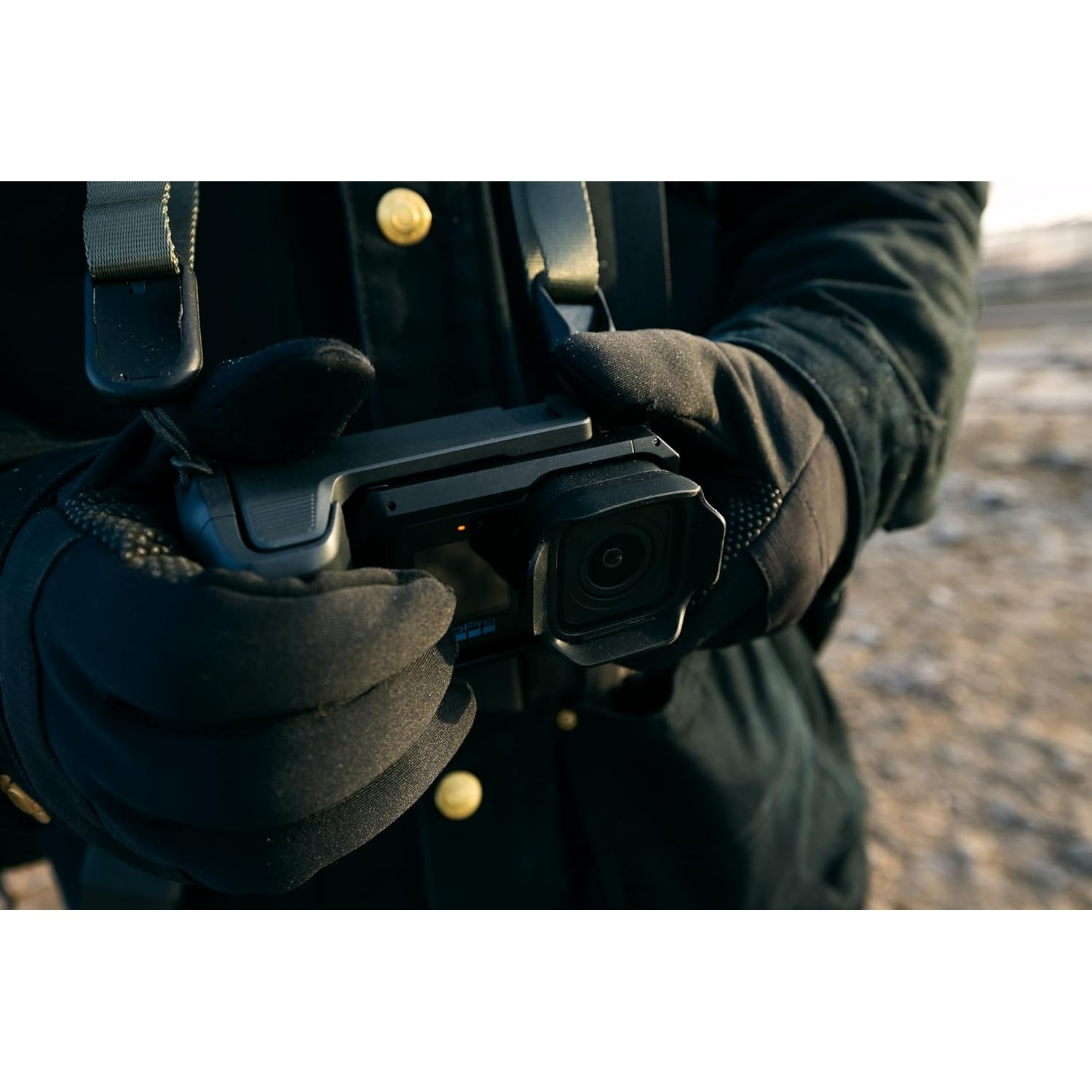 Hands in black gloves hold a black action camera. A strap is visible.
