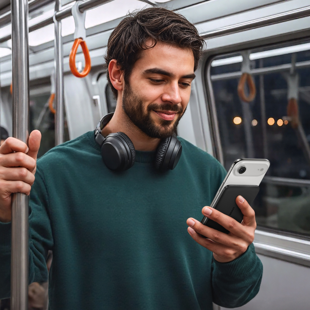 Ein Mann mit Kopfhörern im Zug hält ein Smartphone. Er trägt einen grünen Pullover.
