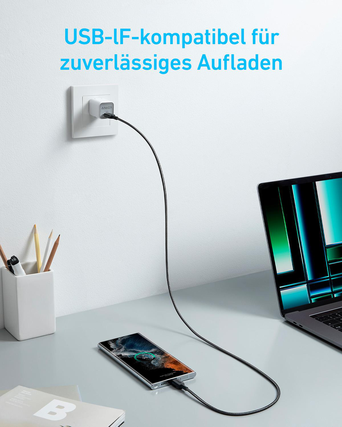 Ein USB-Ladegerät lädt ein Smartphone, das neben einem Laptop liegt.