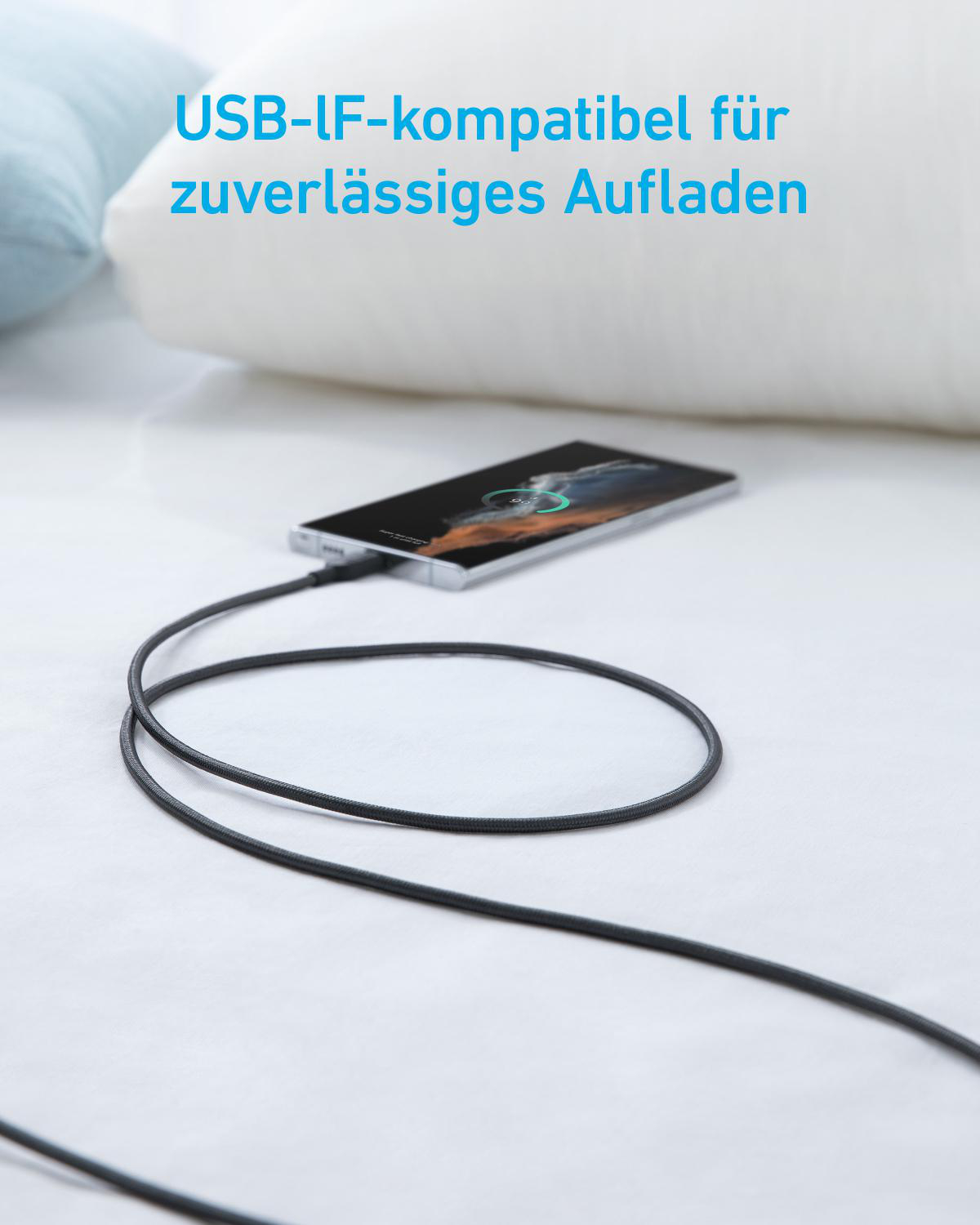 Ein schwarzes Ladekabel verbindet ein Smartphone, das auf einem Bett liegt.