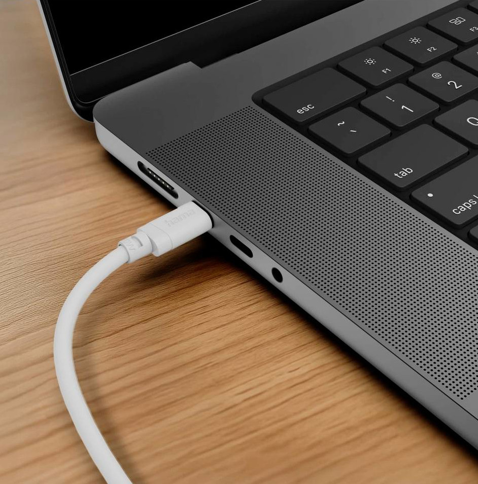 Biały kabel jest podłączony do laptopa leżącego na drewnianym stole.