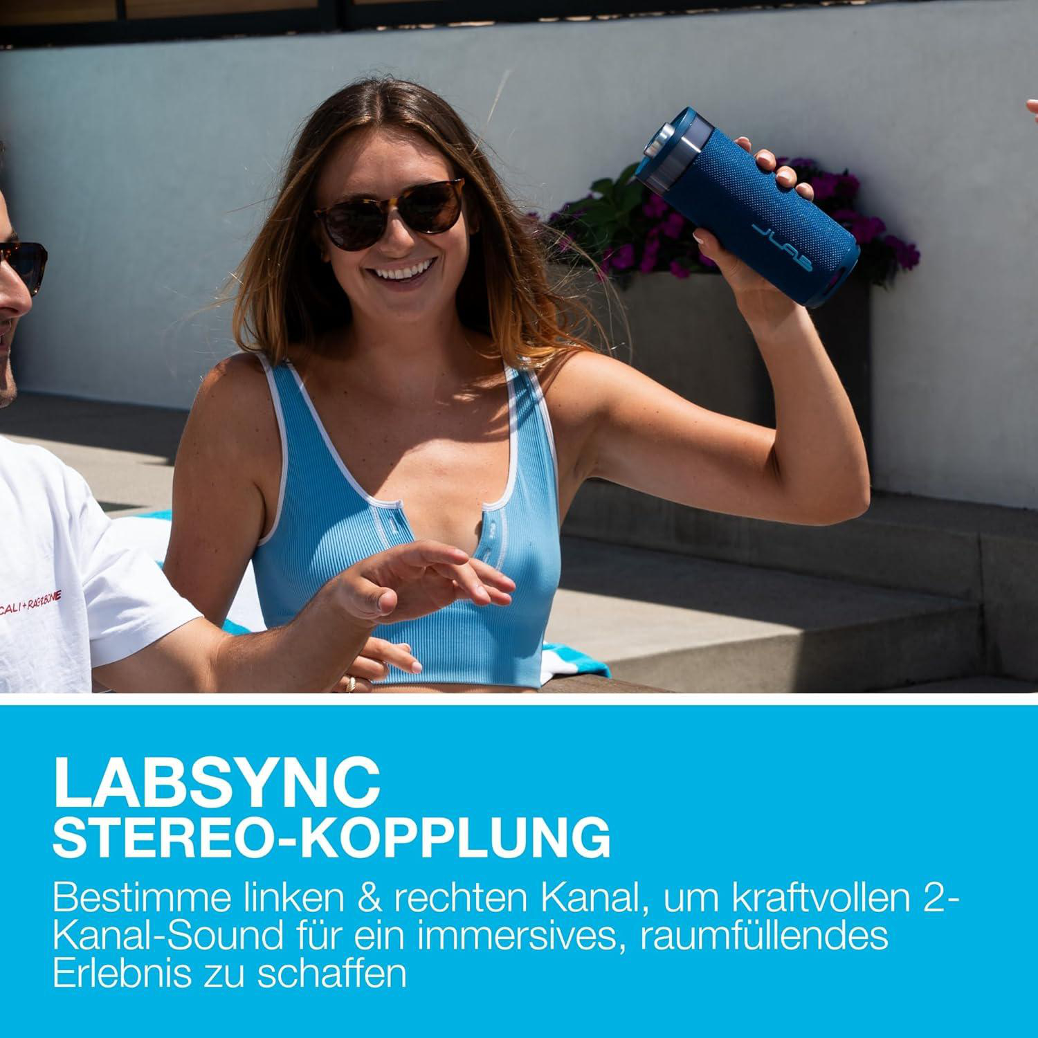 Frau mit Sonnenbrille hält blaue Lautsprecherbox in der Hand, Mann daneben.