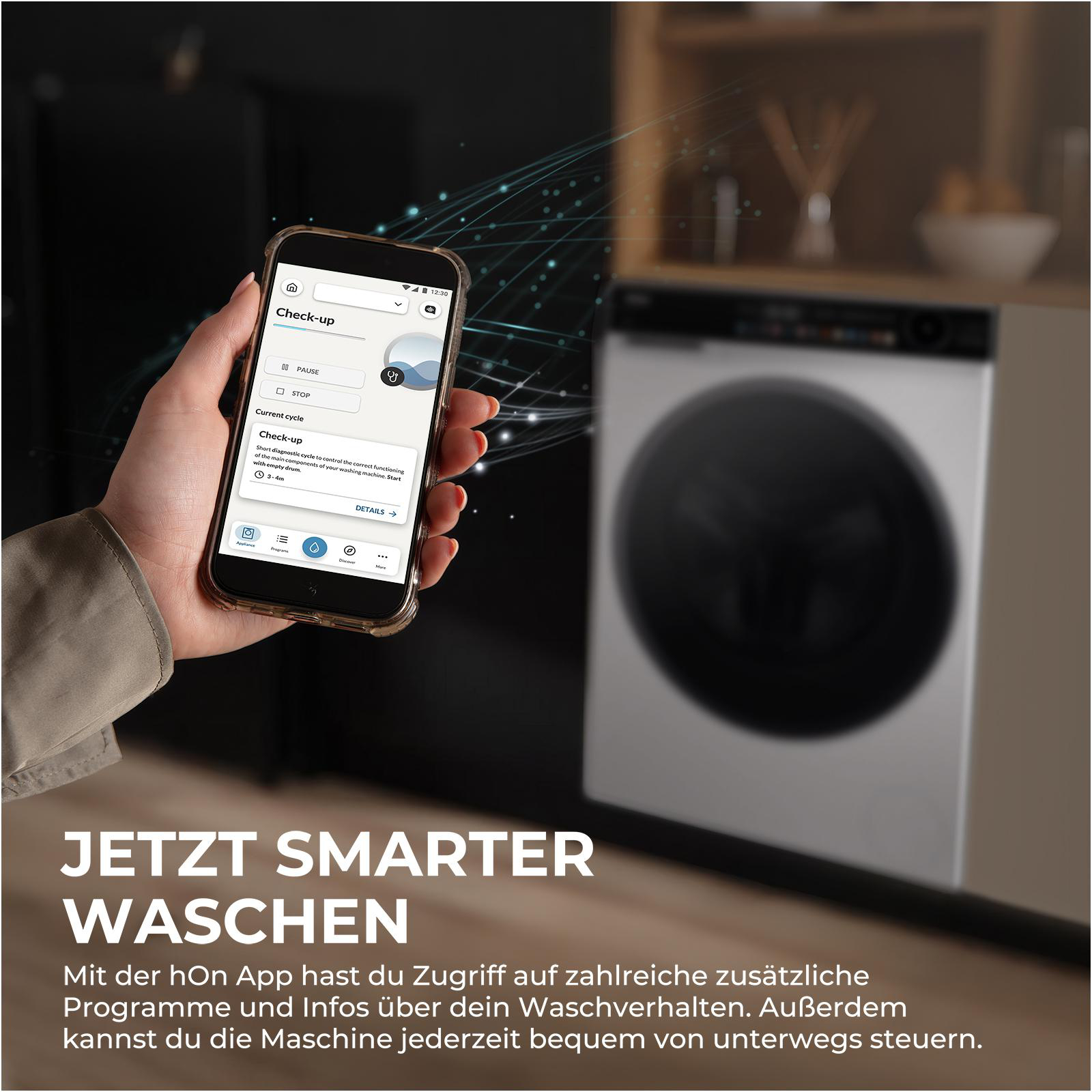 Eine Hand hält ein Smartphone mit einer Waschmaschinen-App. Im Hintergrund eine Waschmaschine.