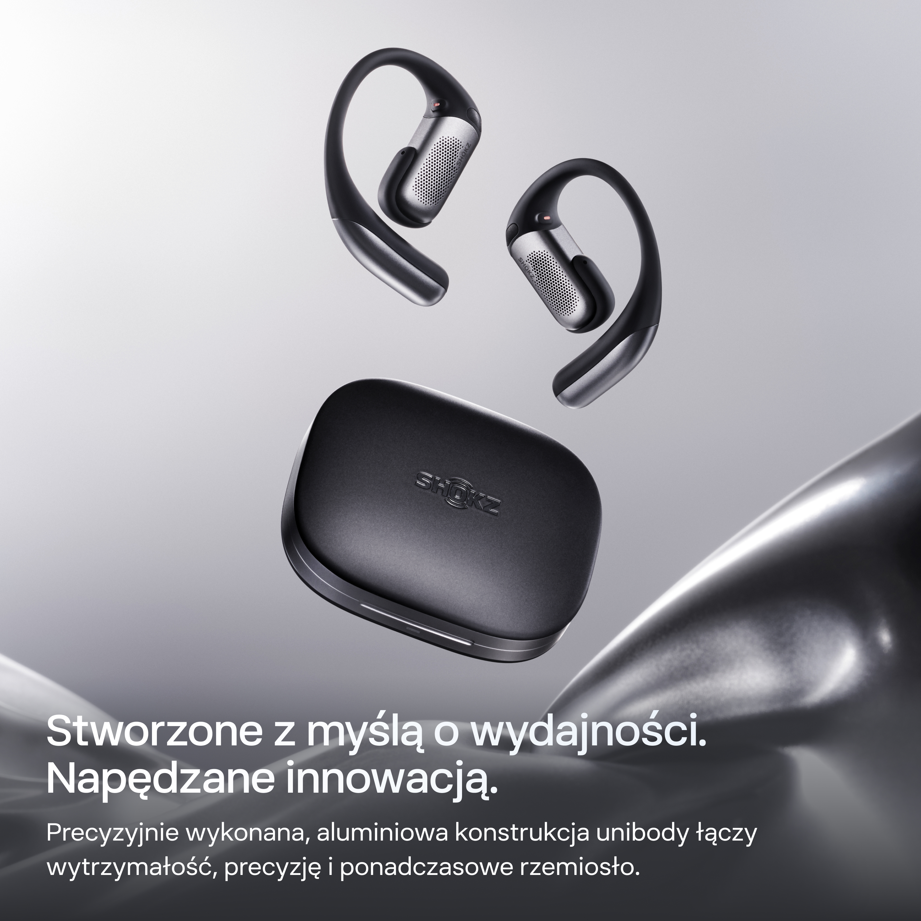 Czarne słuchawki z etui ładującym na szarym tle.