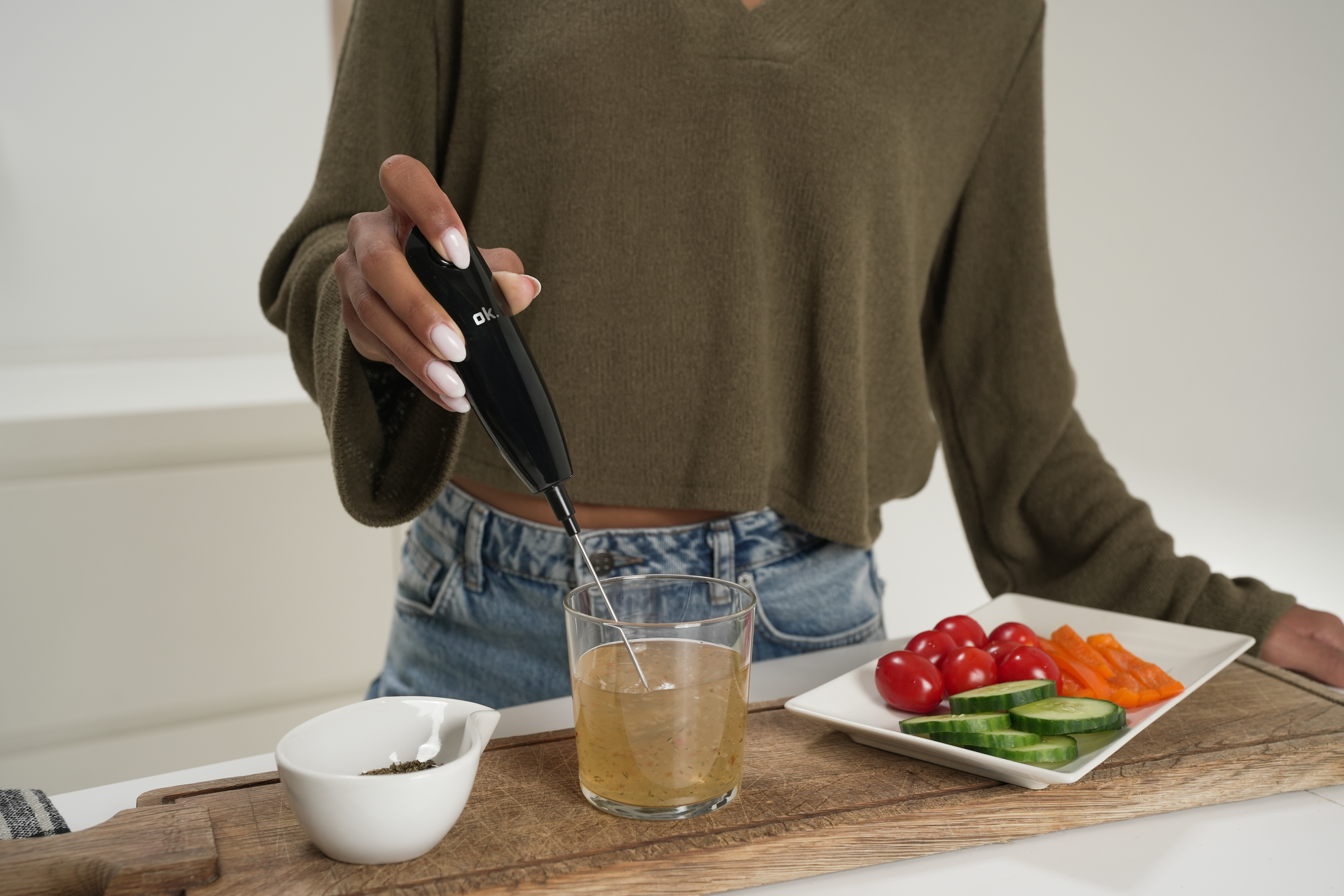 Una mano sostiene un espumador de leche negro en un vaso con líquido.