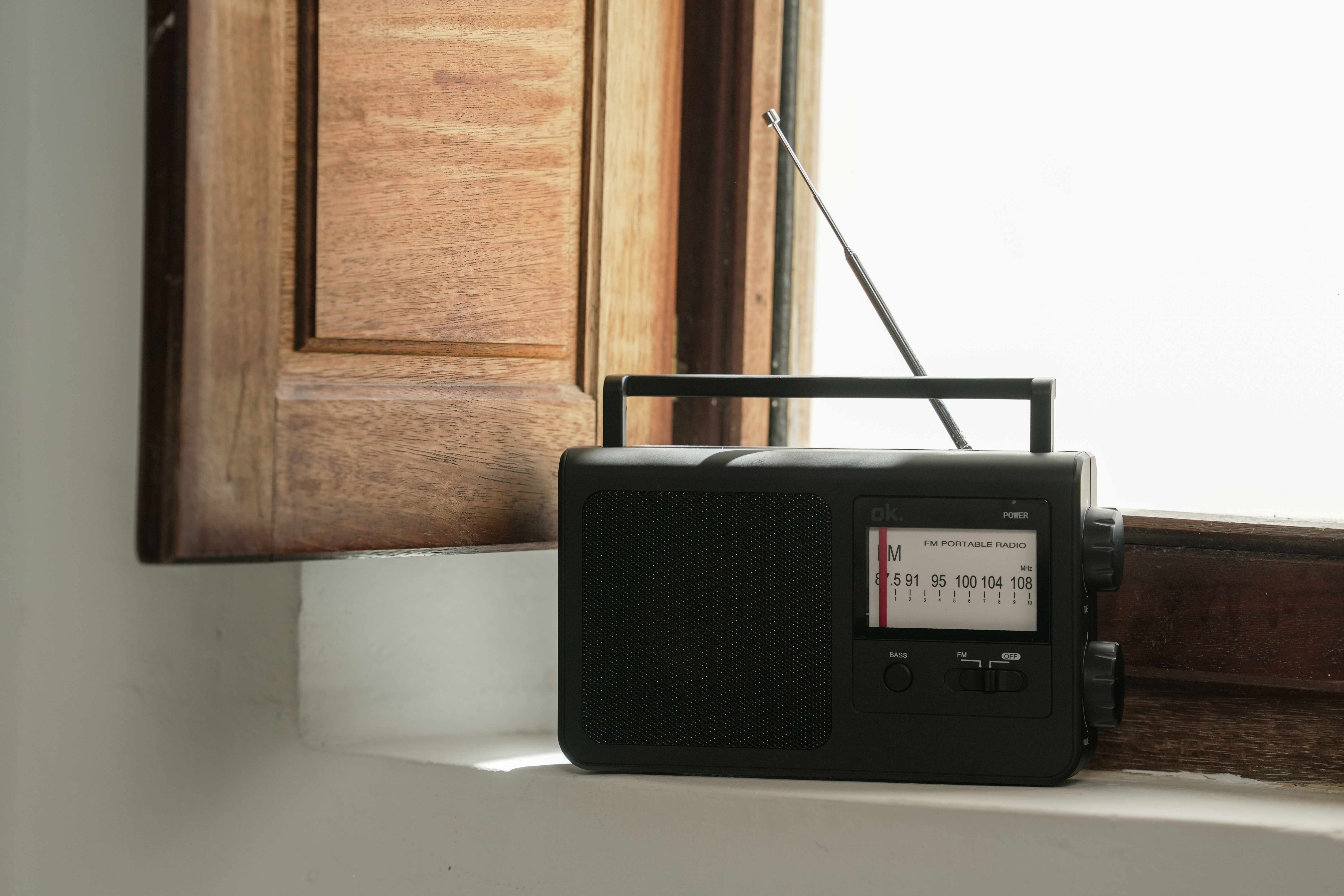 Czarno-przenośne radio z anteną stoi na parapecie obok drewnianej boazerii.