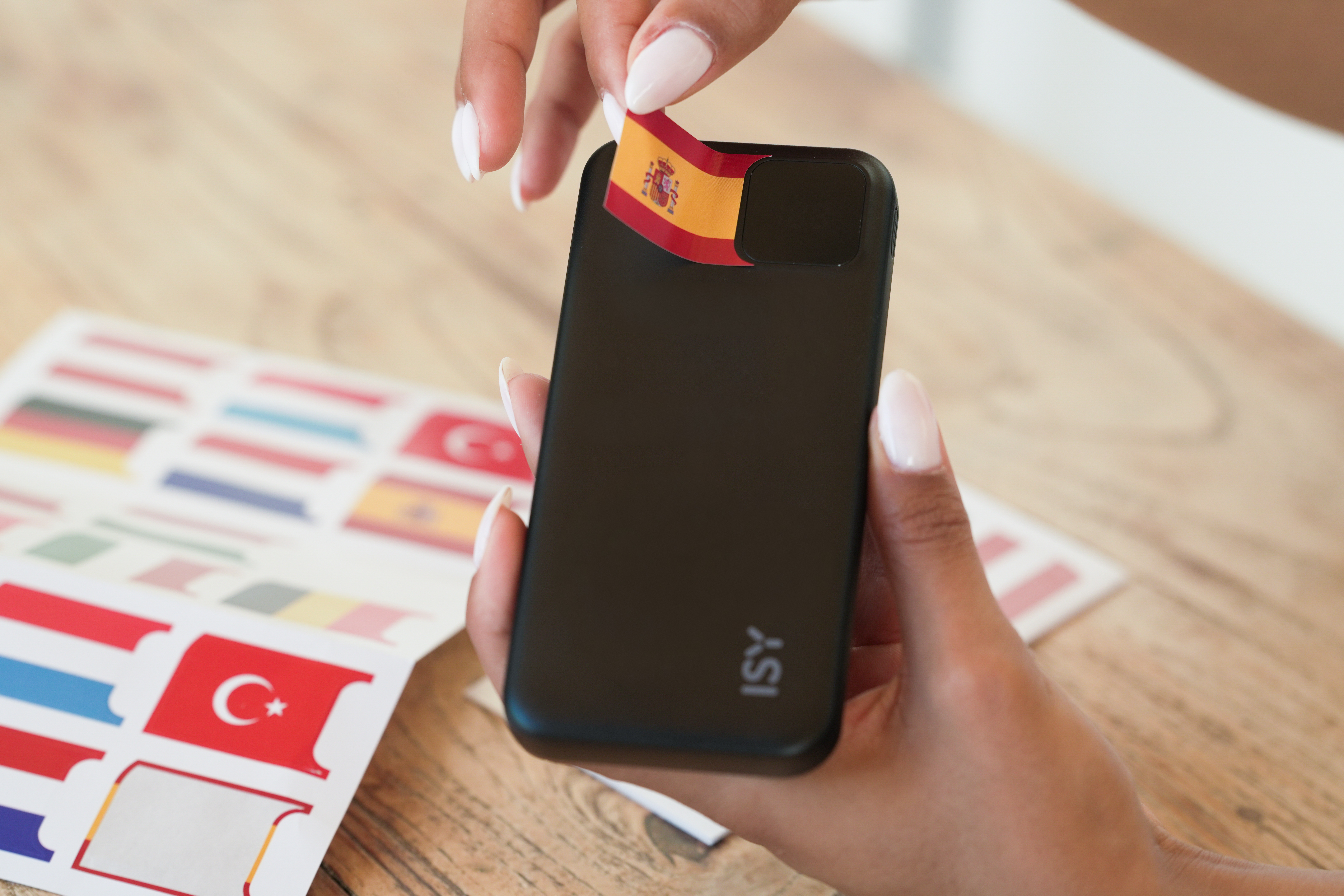 Eine Hand platziert eine spanische Flagge auf einem schwarzen Handy.