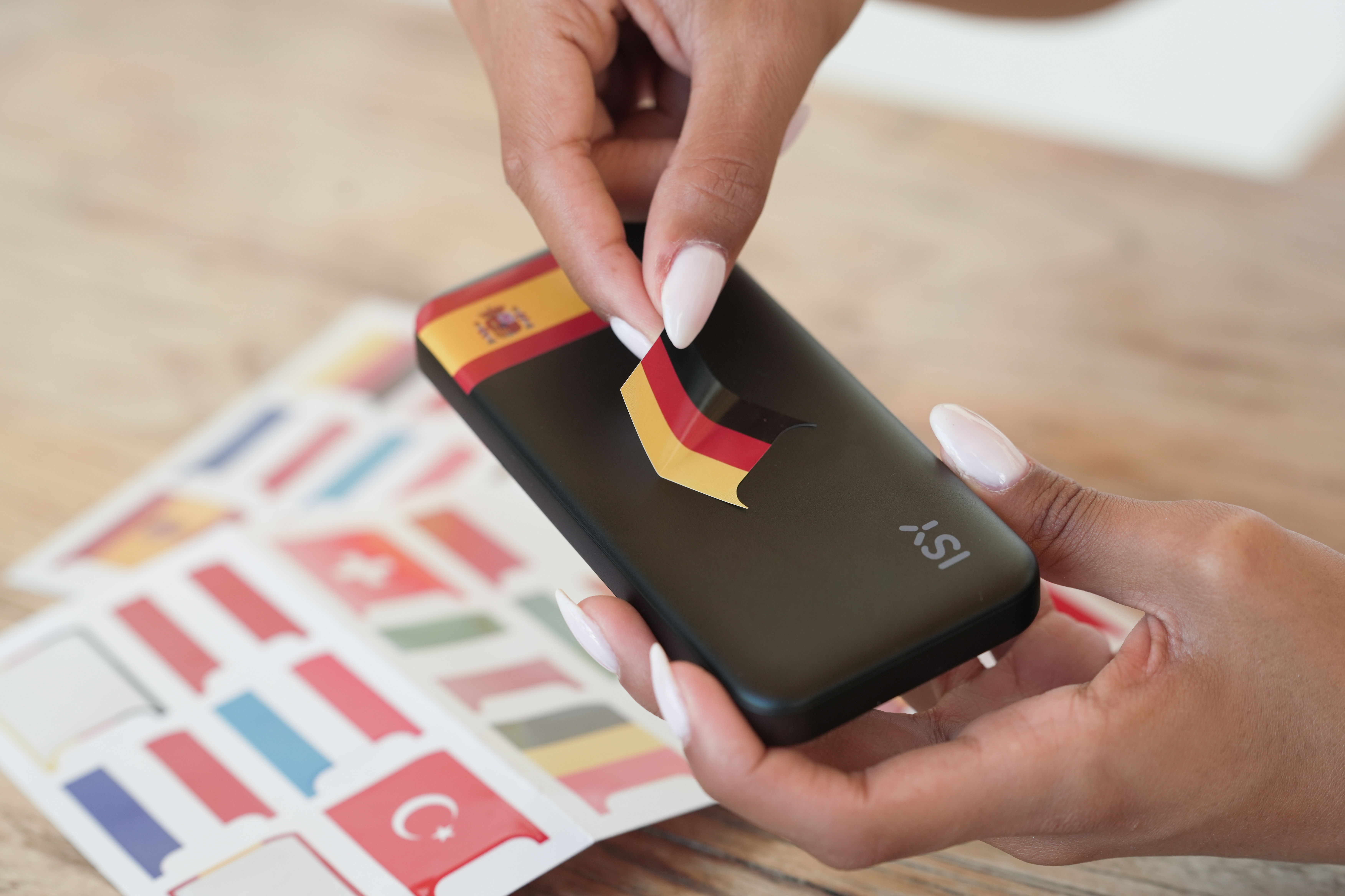 Eine Hand klebt eine Deutschlandflagge auf ein dunkles Handy, daneben liegen Flaggenaufkleber.