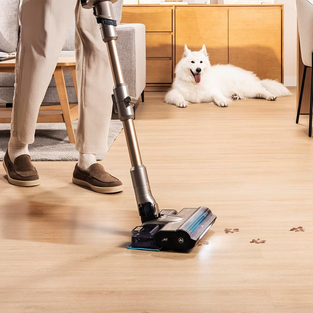 Beyaz bir köpek yerde yatarken bir kişi ahşap zemini süpürüyor.