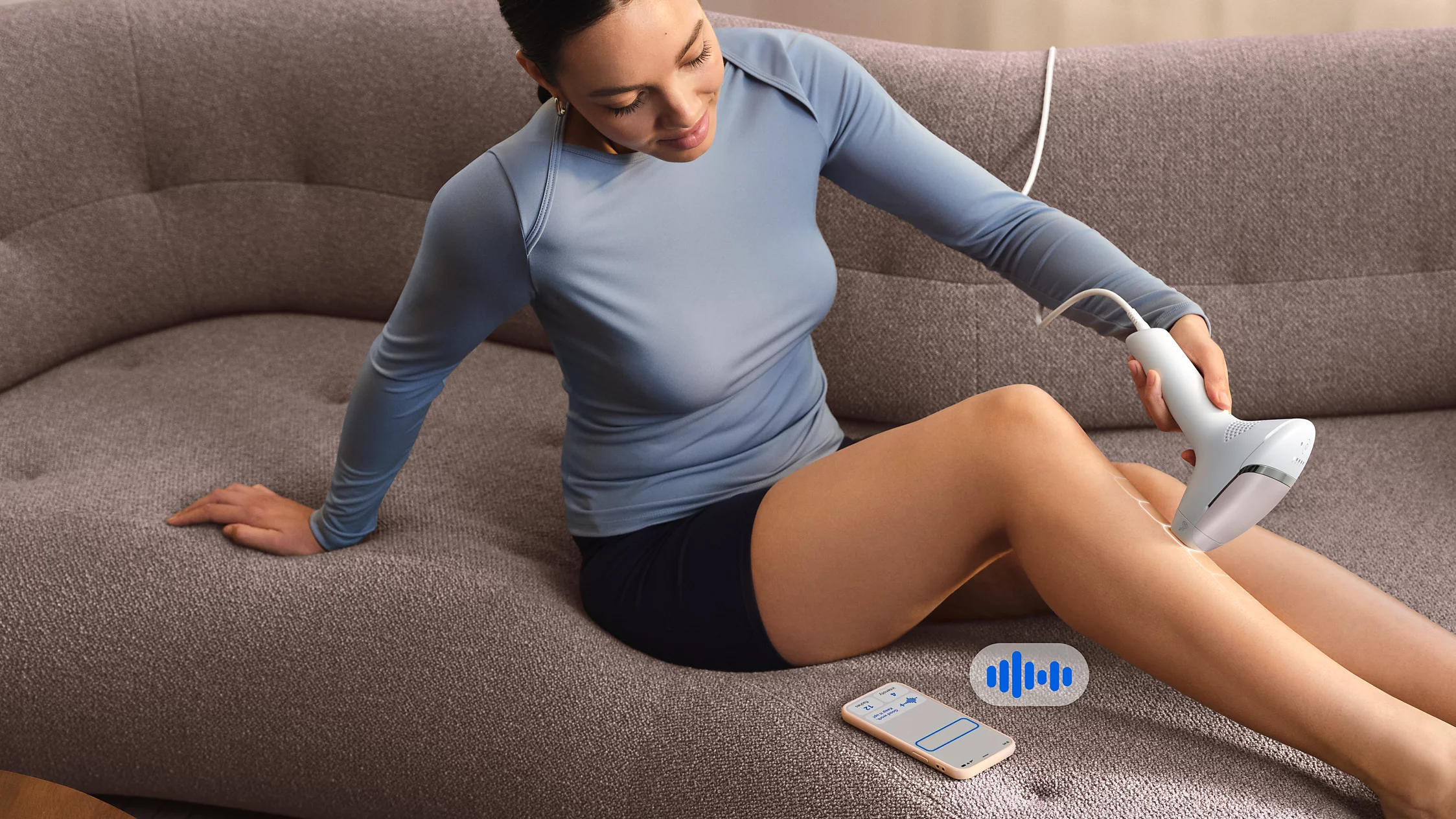 Eine Frau benutzt ein IPL-Gerät an ihrem Bein, während sie auf einem Sofa sitzt.