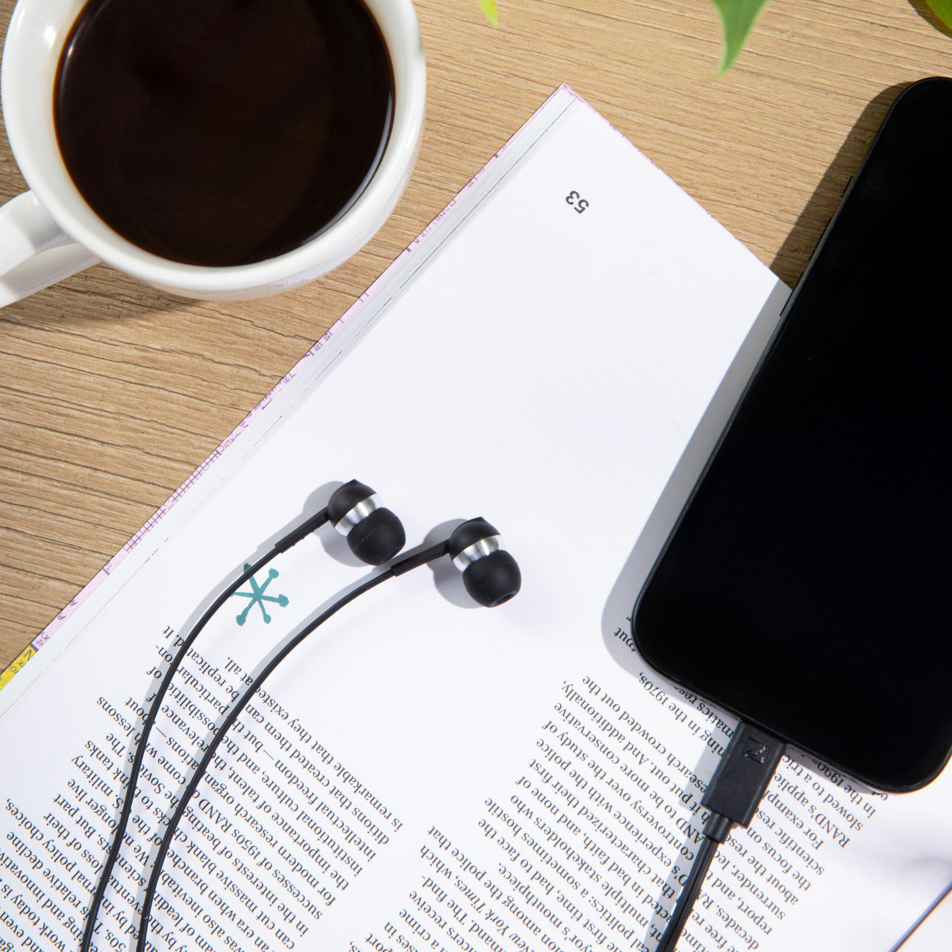 Bir fincan kahve, akıllı telefon ve kulaklık bir dergi üzerinde.