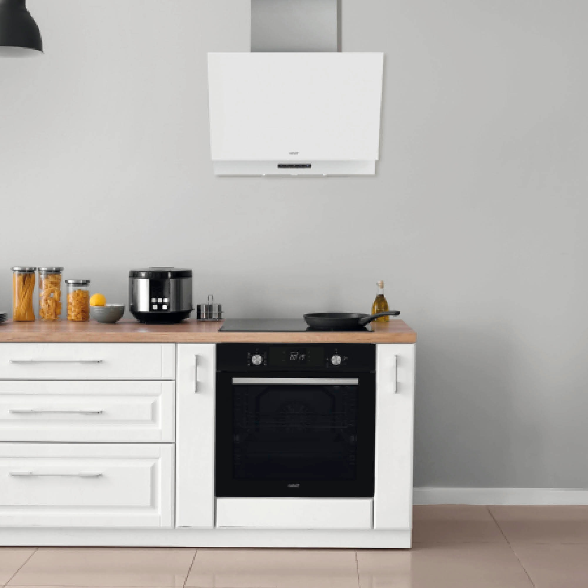 Cocina moderna con gabinetes blancos, horno empotrado, campana y utensilios.