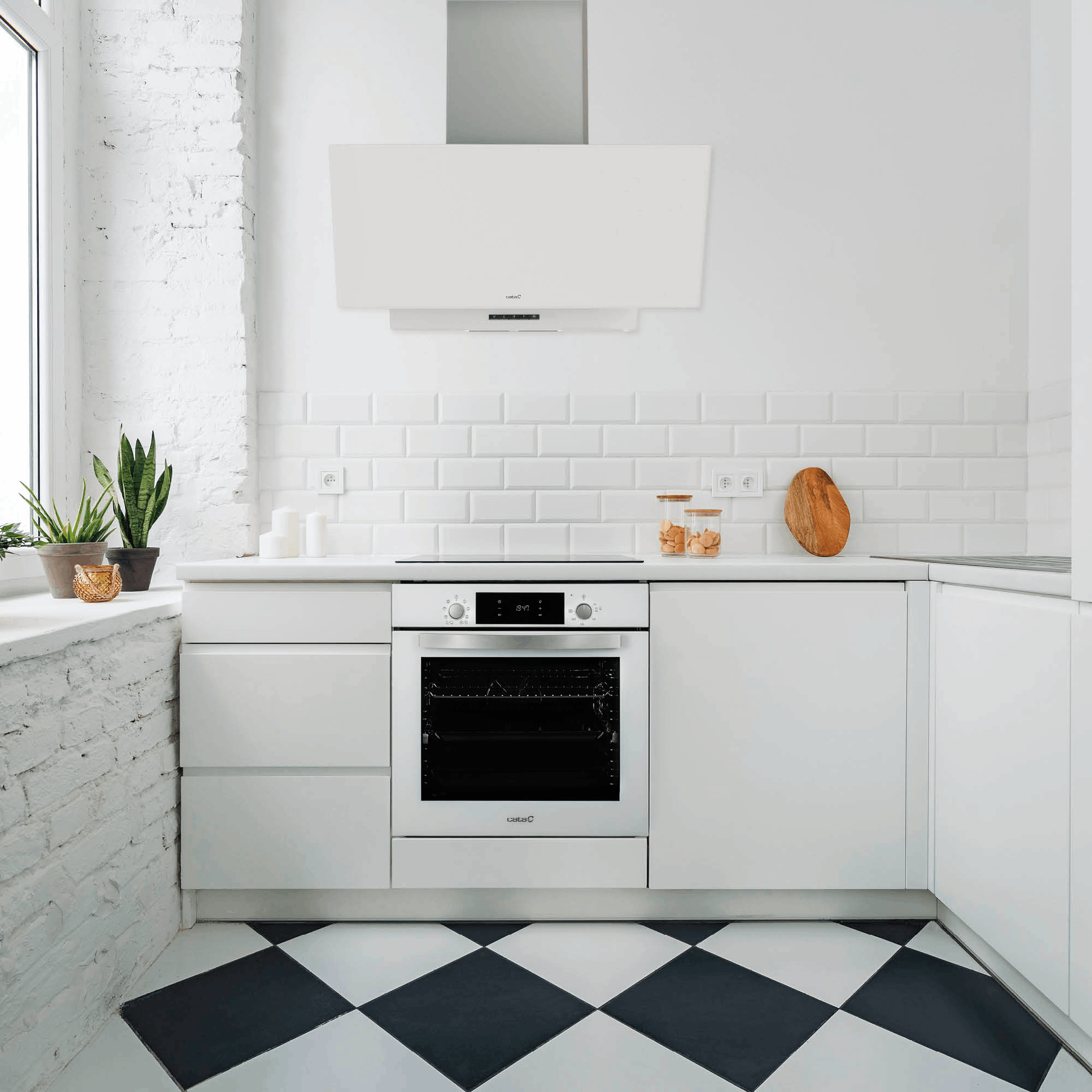 Cocina blanca moderna con horno, campana, plantas y baldosas de suelo blancas y negras.