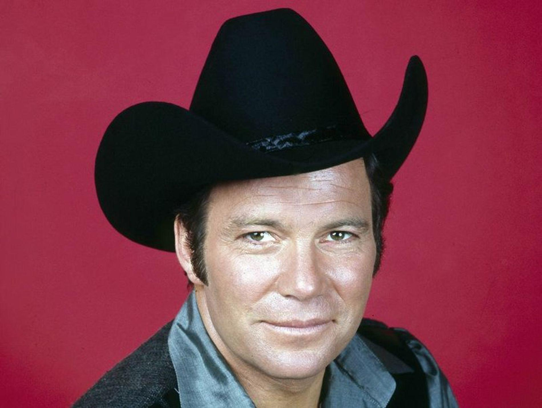 Mann mit schwarzem Cowboyhut und grauem Hemd vor rotem Hintergrund.