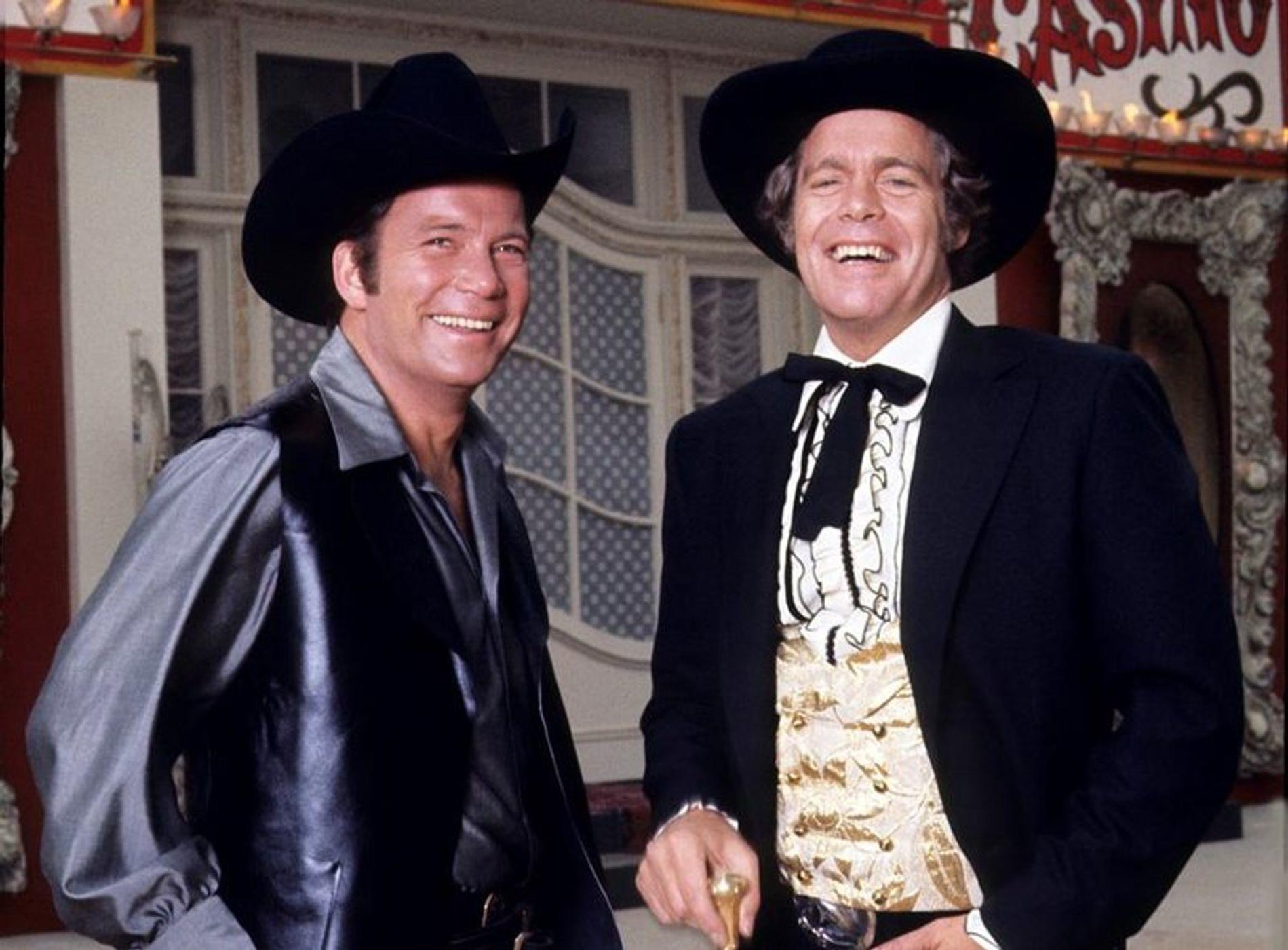 Zwei Männer in Cowboyhüten und Westernkleidung lächeln in die Kamera.