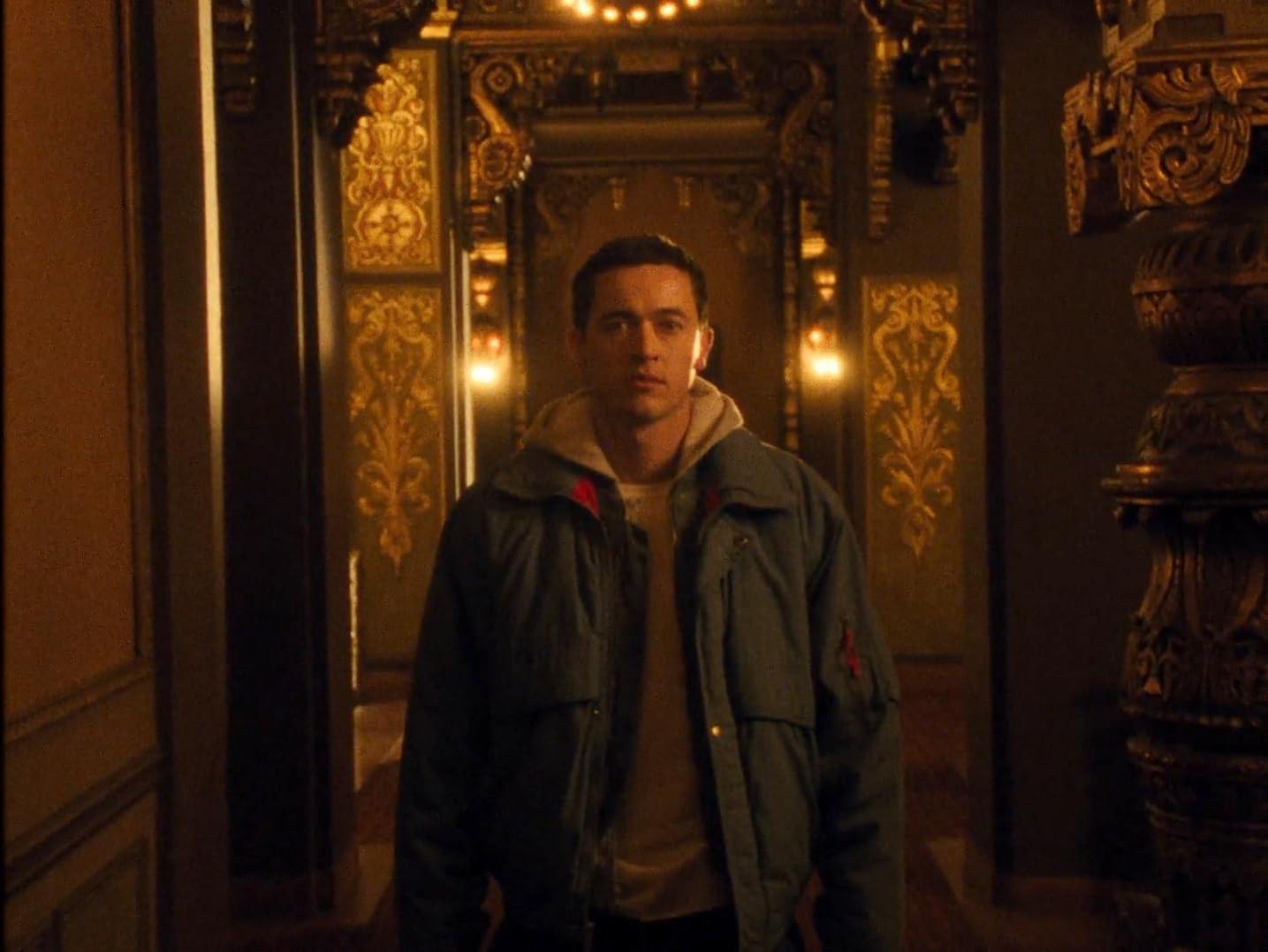 Ein Mann in einer Jacke steht in einem opulenten Flur mit goldenen Verzierungen.