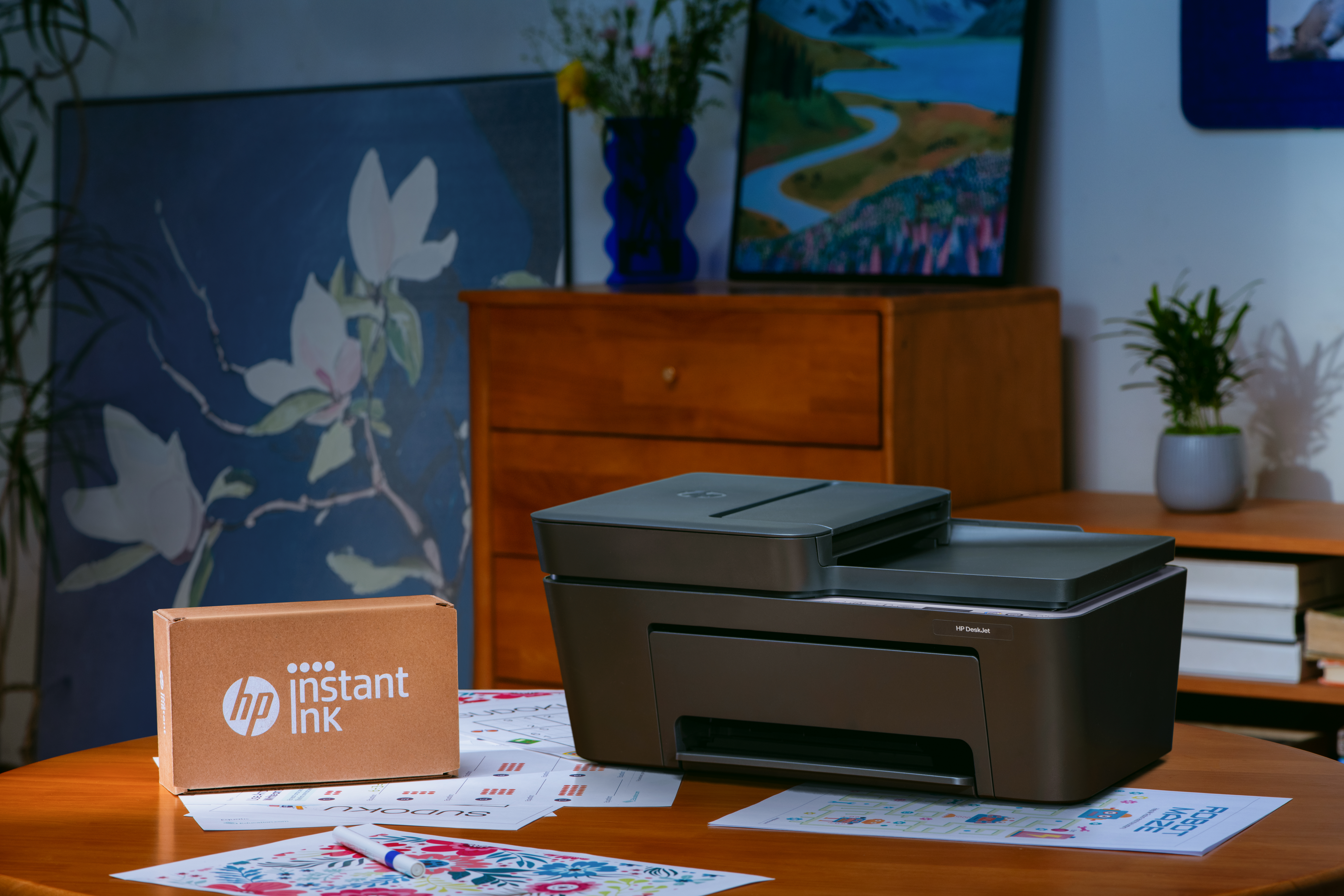 Ein Drucker steht auf einem Holztisch neben einer HP Instant Ink Box.