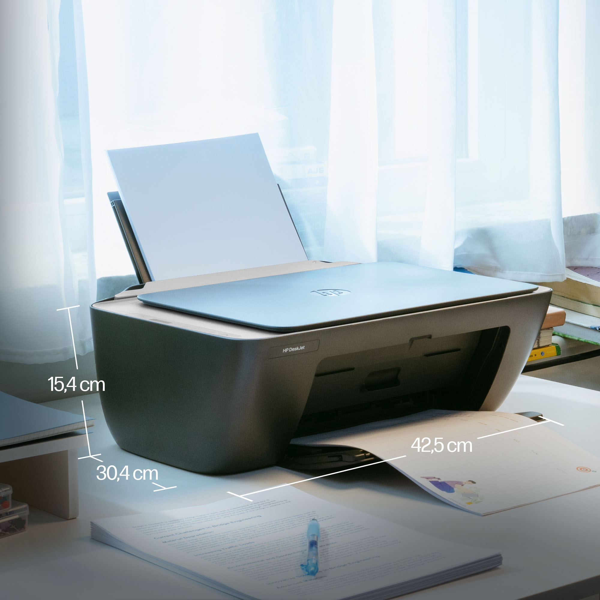 Ein grauer HP DeskJet Drucker steht auf einem Schreibtisch mit Papier und Büchern.