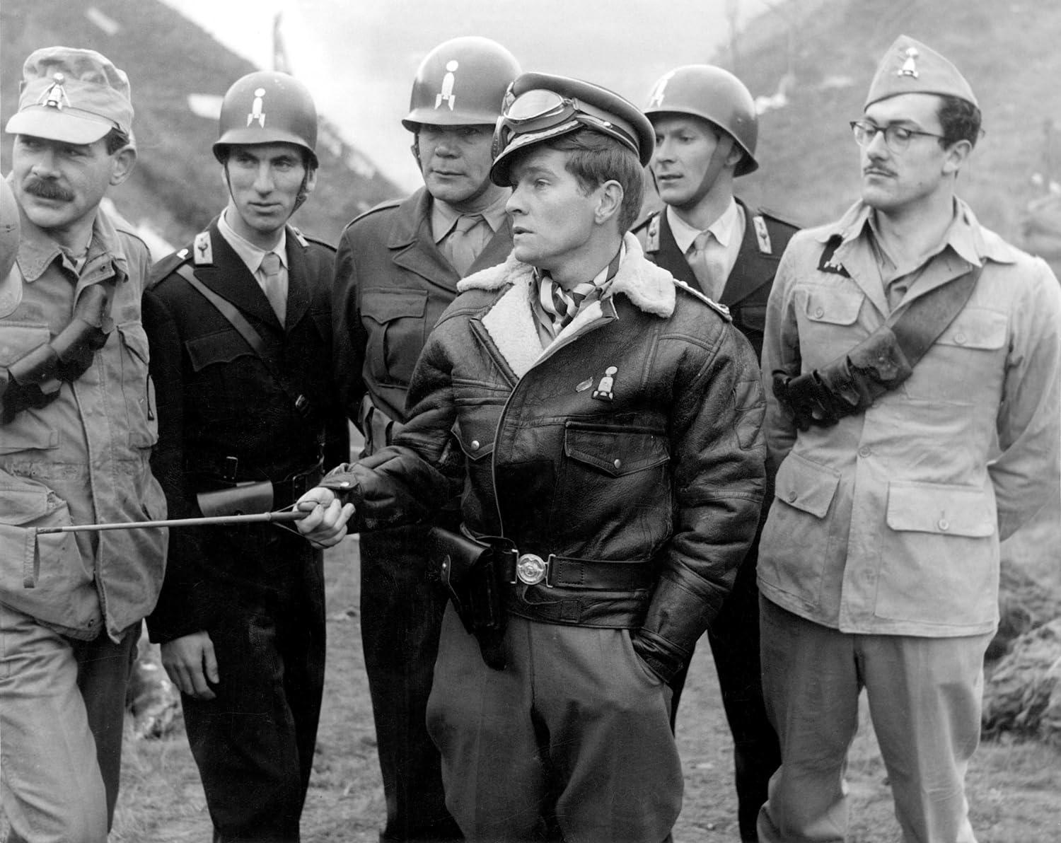 Sechs Männer in Uniformen und Helmen stehen im Freien. Einer hält einen Stock.