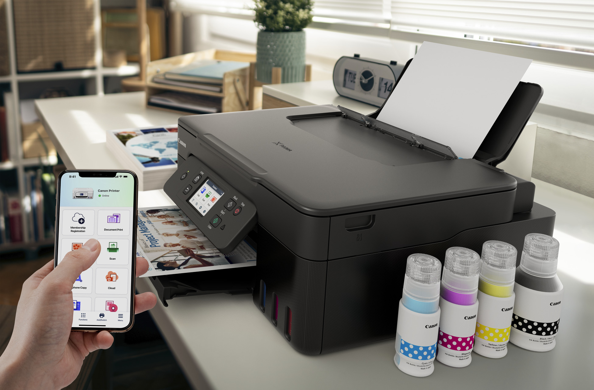 Uno smartphone mostra l'app Canon accanto a una stampante con flaconi d'inchiostro.