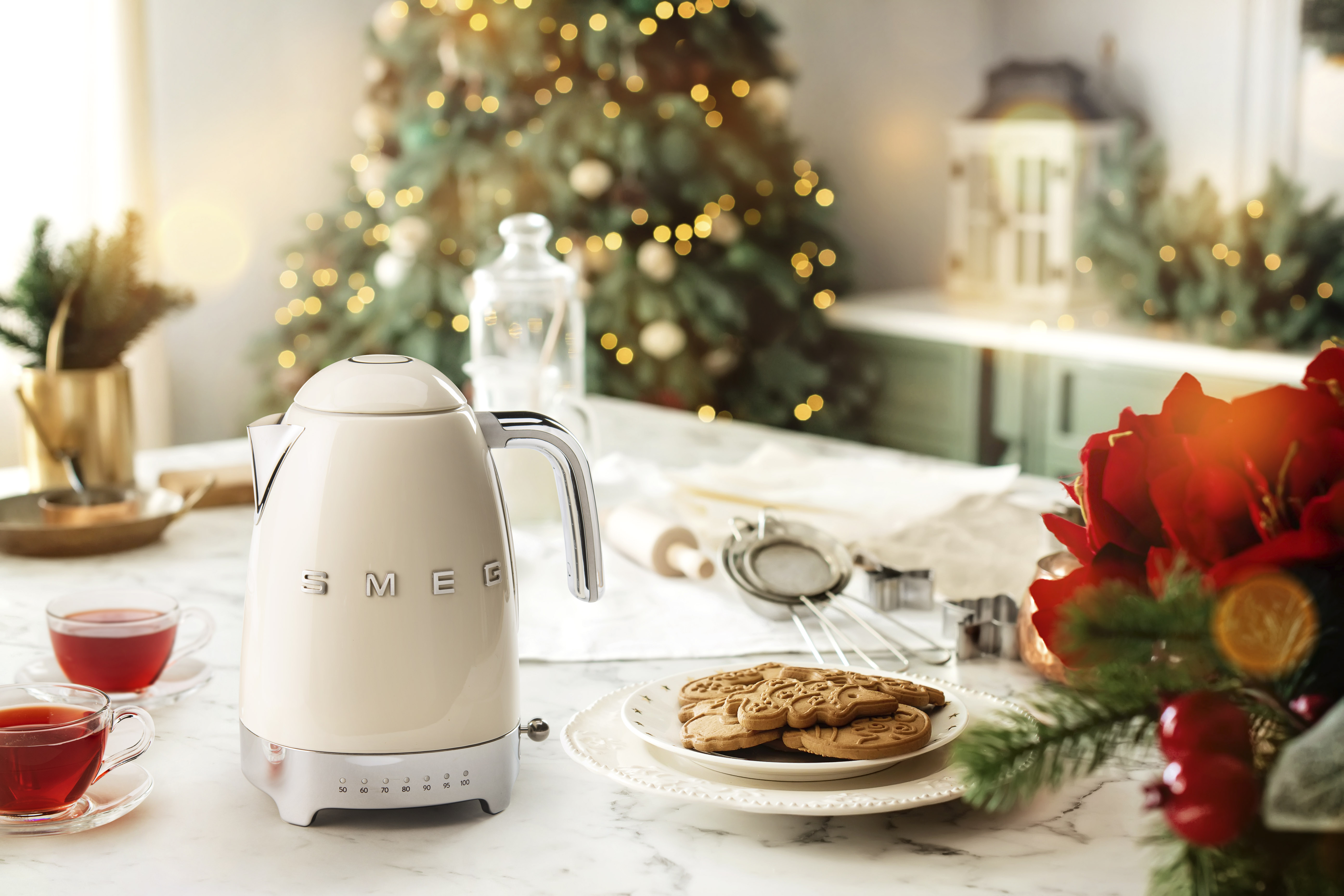 Eine cremefarbene Smeg-Kanne, zwei Tassen Tee, Kekse und Weihnachtsdeko.