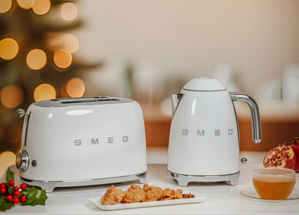Ein weißer SMEG-Toaster und Wasserkocher stehen auf einer Tischplatte. Im Hintergrund sind Lichter zu sehen.