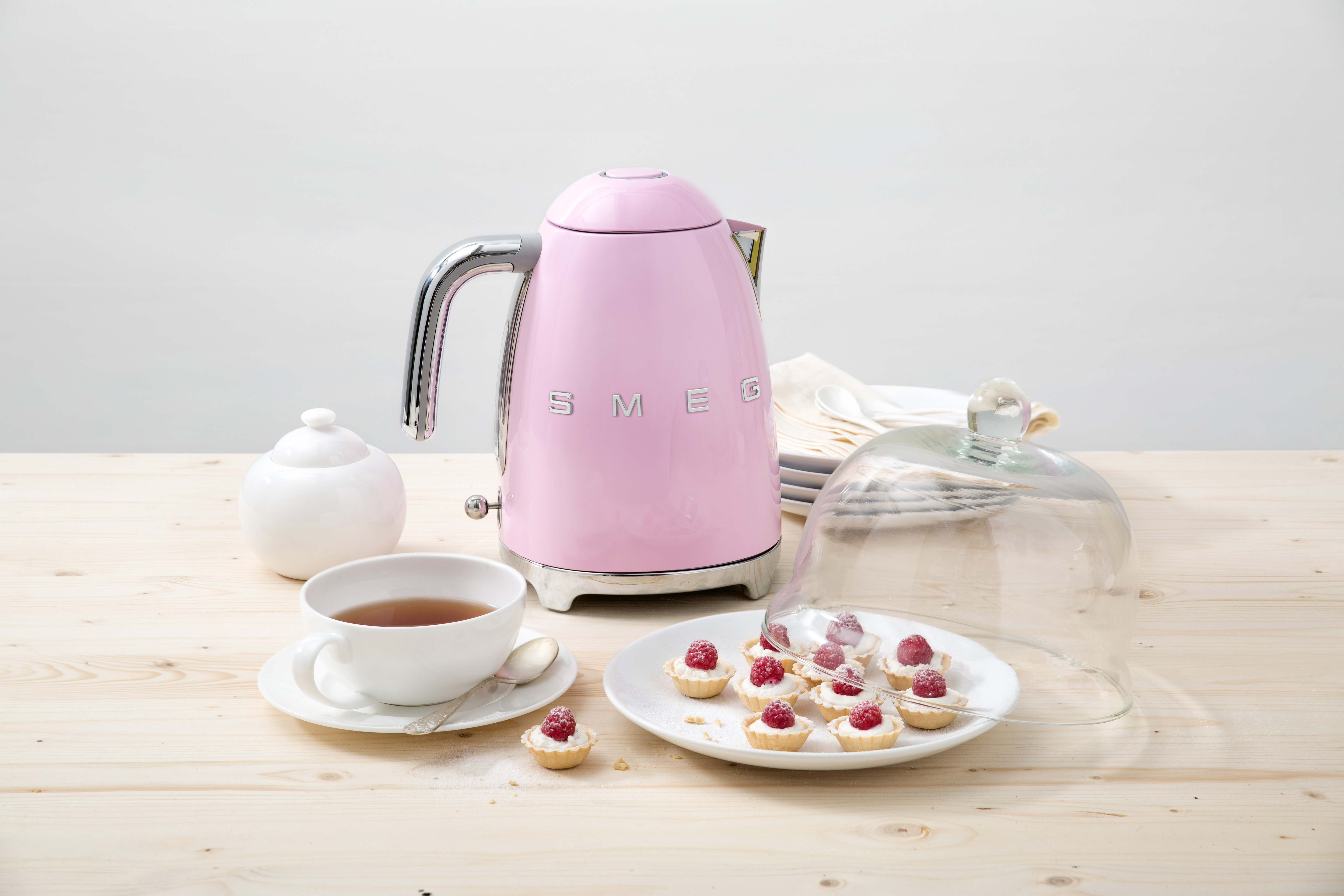 Ein rosafarbener Smeg-Wasserkocher mit Tasse, Zuckerdose und Kuchen.
