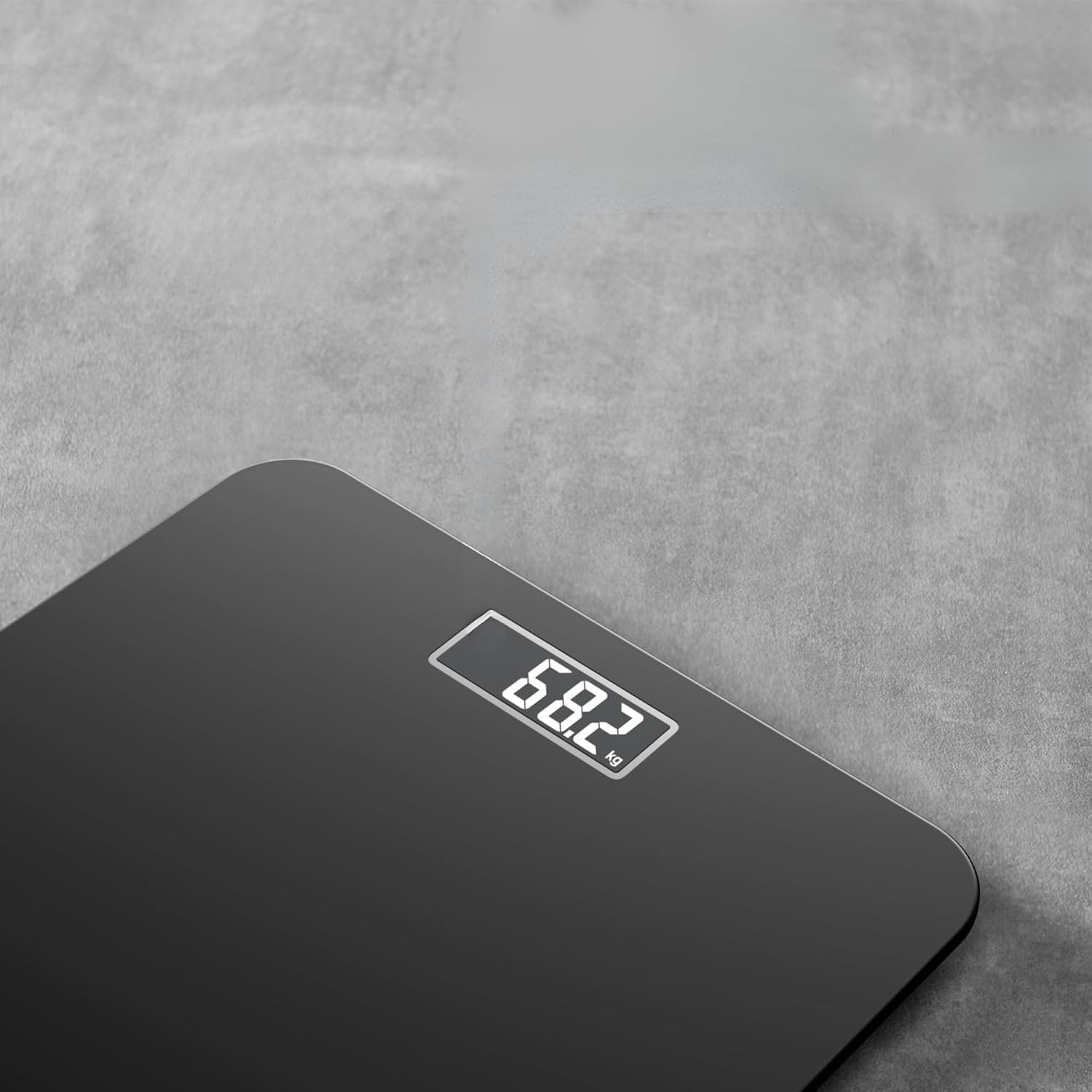 Eine schwarze Digitalwaage zeigt 68,2 kg auf einer grauen Betonoberfläche an.