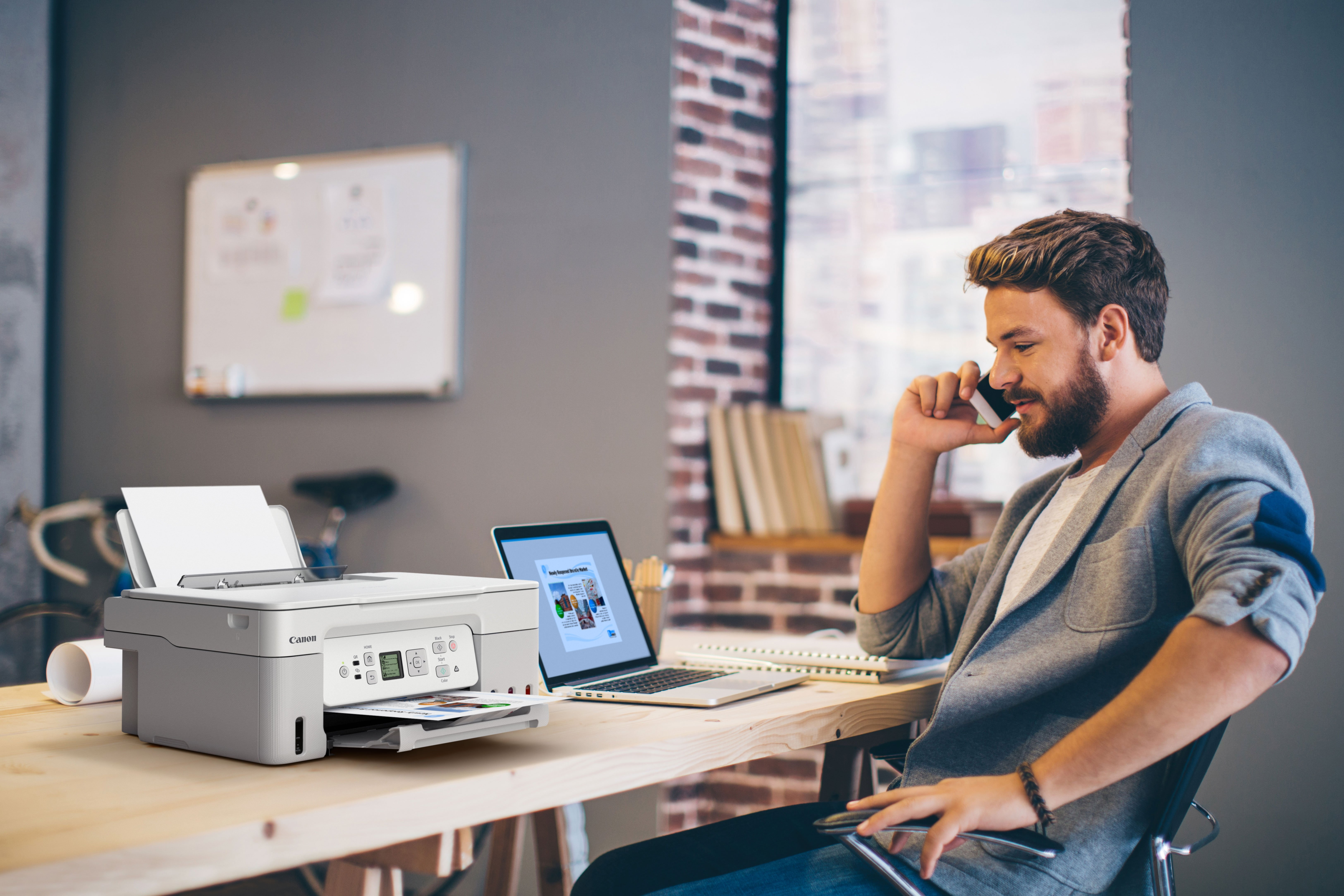 Mann telefoniert am Schreibtisch neben Drucker und Laptop.