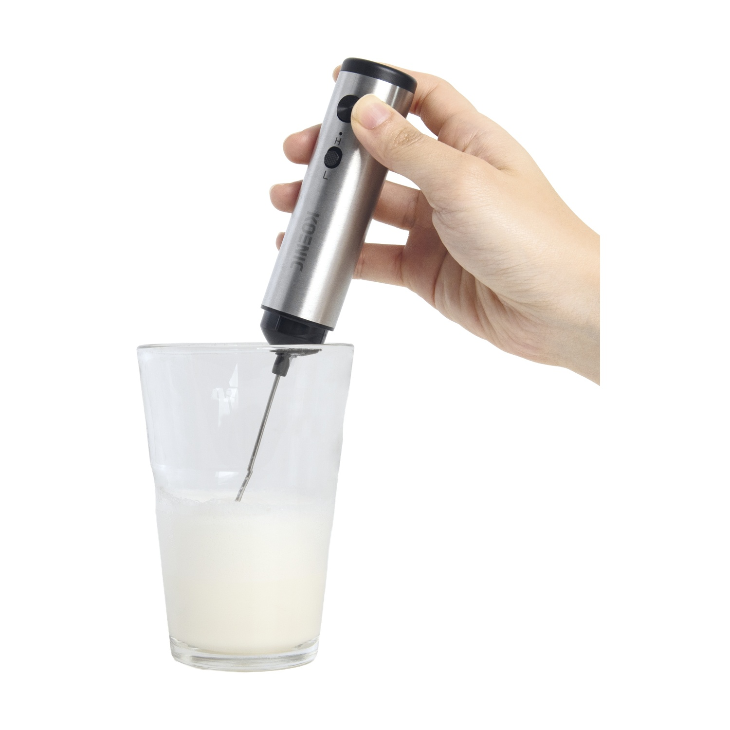 Mano tiene montalatte argentato sopra bicchiere con latte montato.