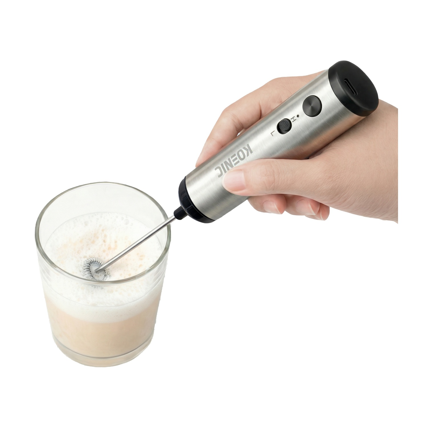 Una mano tiene un montalatte argentato sopra un bicchiere di latte montato.
