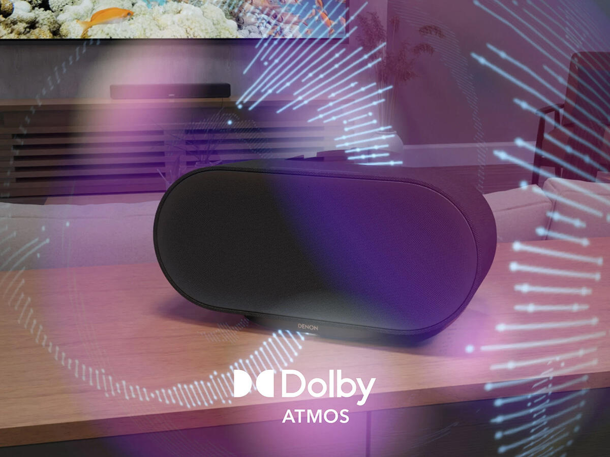 Fekete ovális hangszóró faasztalon Dolby Atmos grafikával.