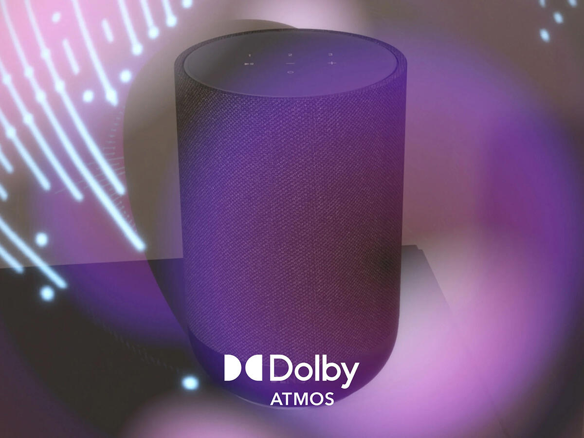 Lila hangszóró Dolby Atmos logóval, világító fények előtt.