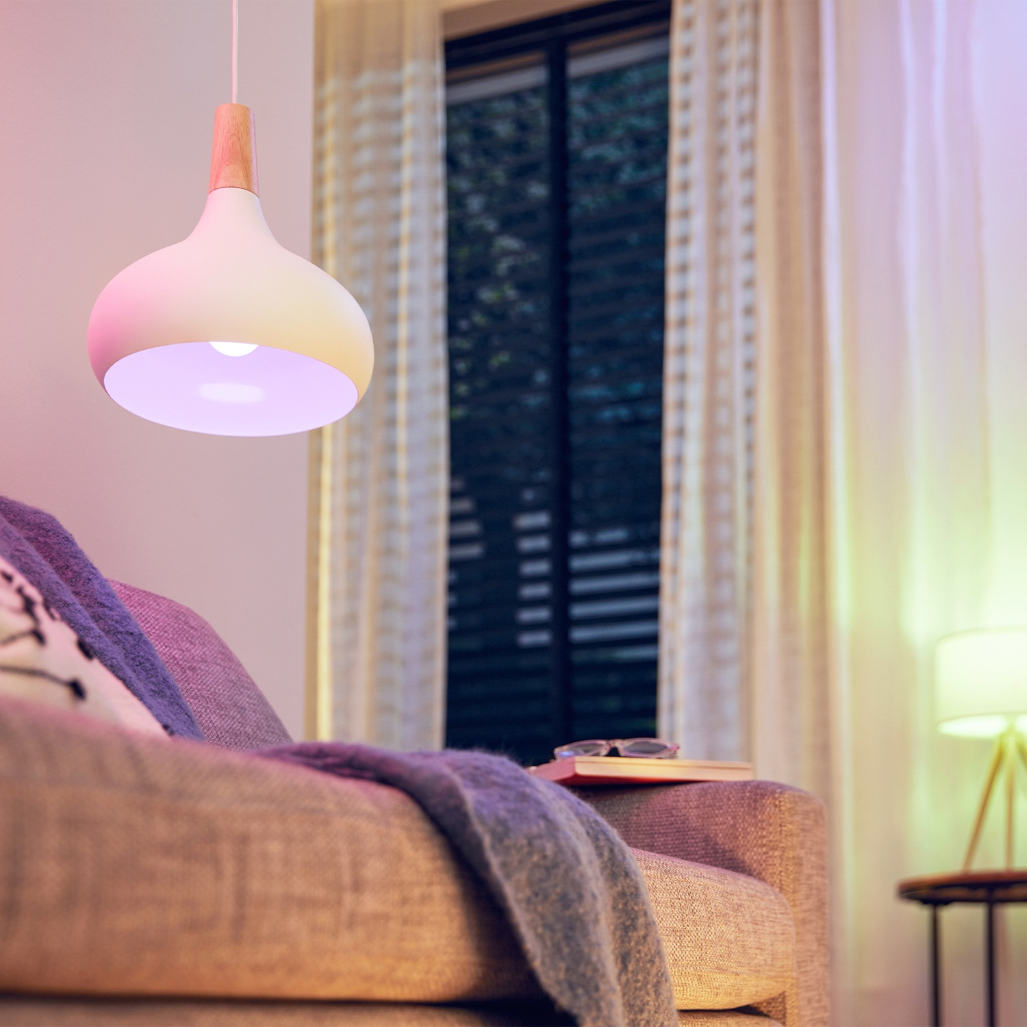 Une suspension moderne avec abat-jour blanc et accent en bois suspendue au-dessus d'un canapé avec couverture violette.