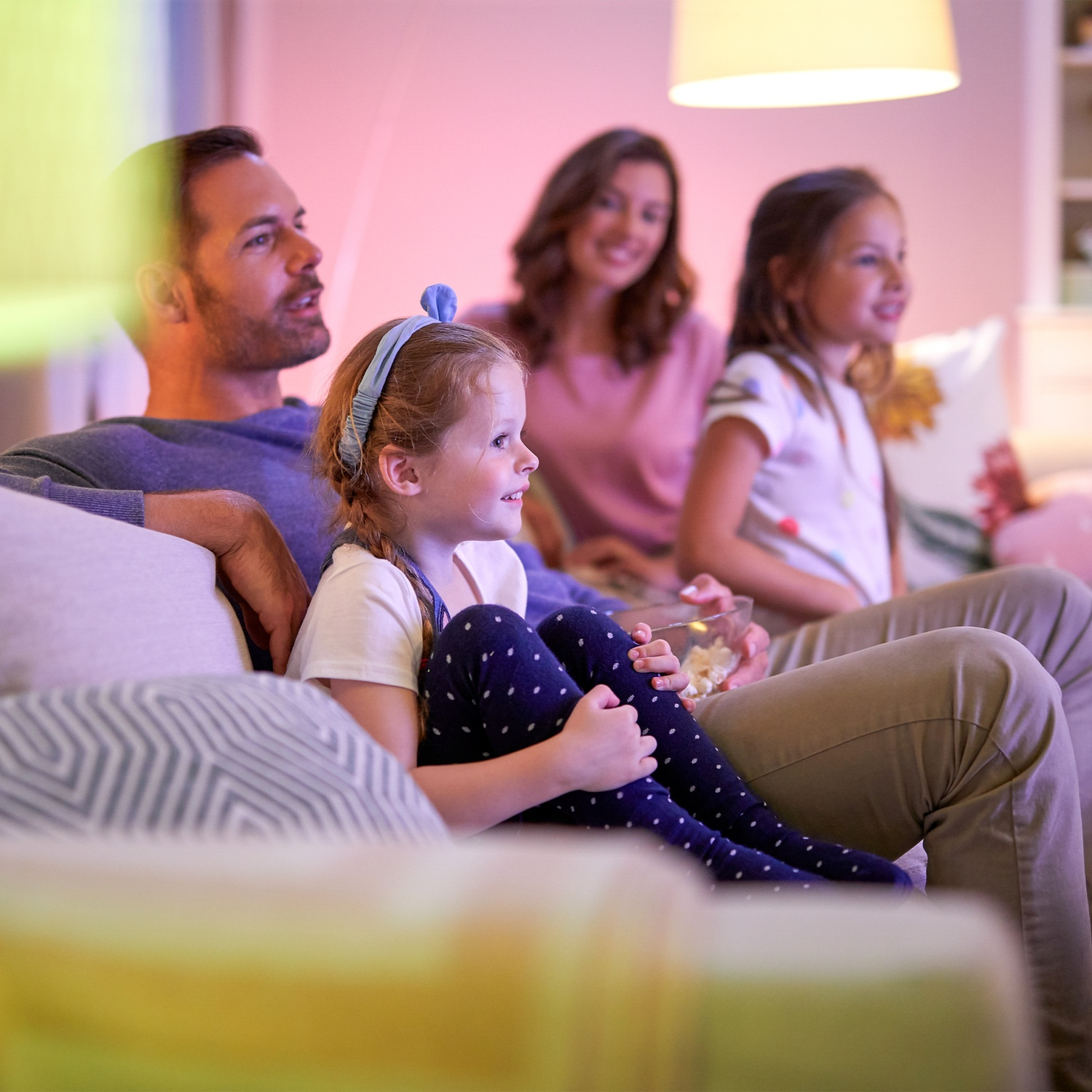 Une famille assise sur un canapé regardant la télé et mangeant du pop-corn.