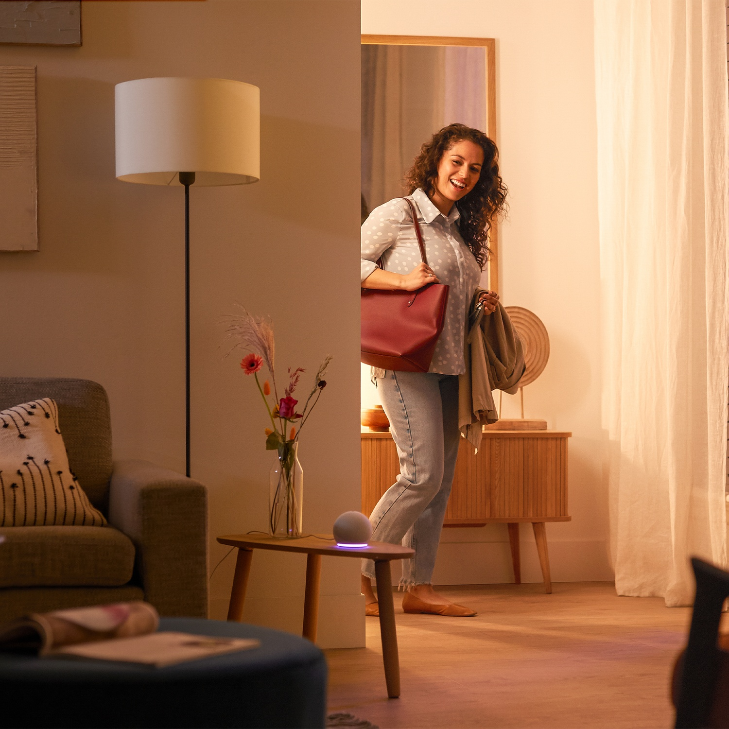 Une femme avec sac et clés entre dans une pièce avec lampe et décor.