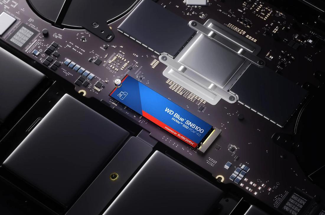 Eine blaue SSD mit rotem Streifen liegt auf einer dunklen Platine mit vielen Chips.