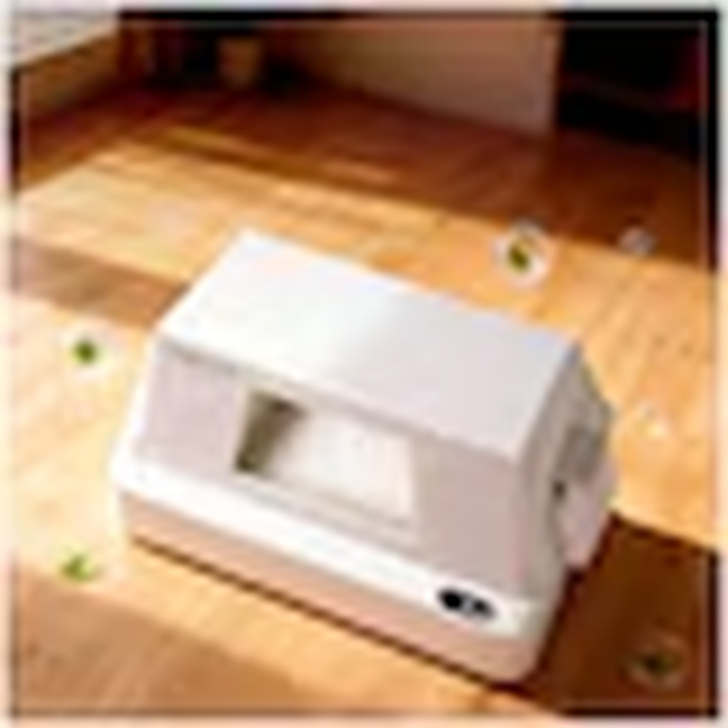 A beige air purifier sits on a wooden floor in sunlight.