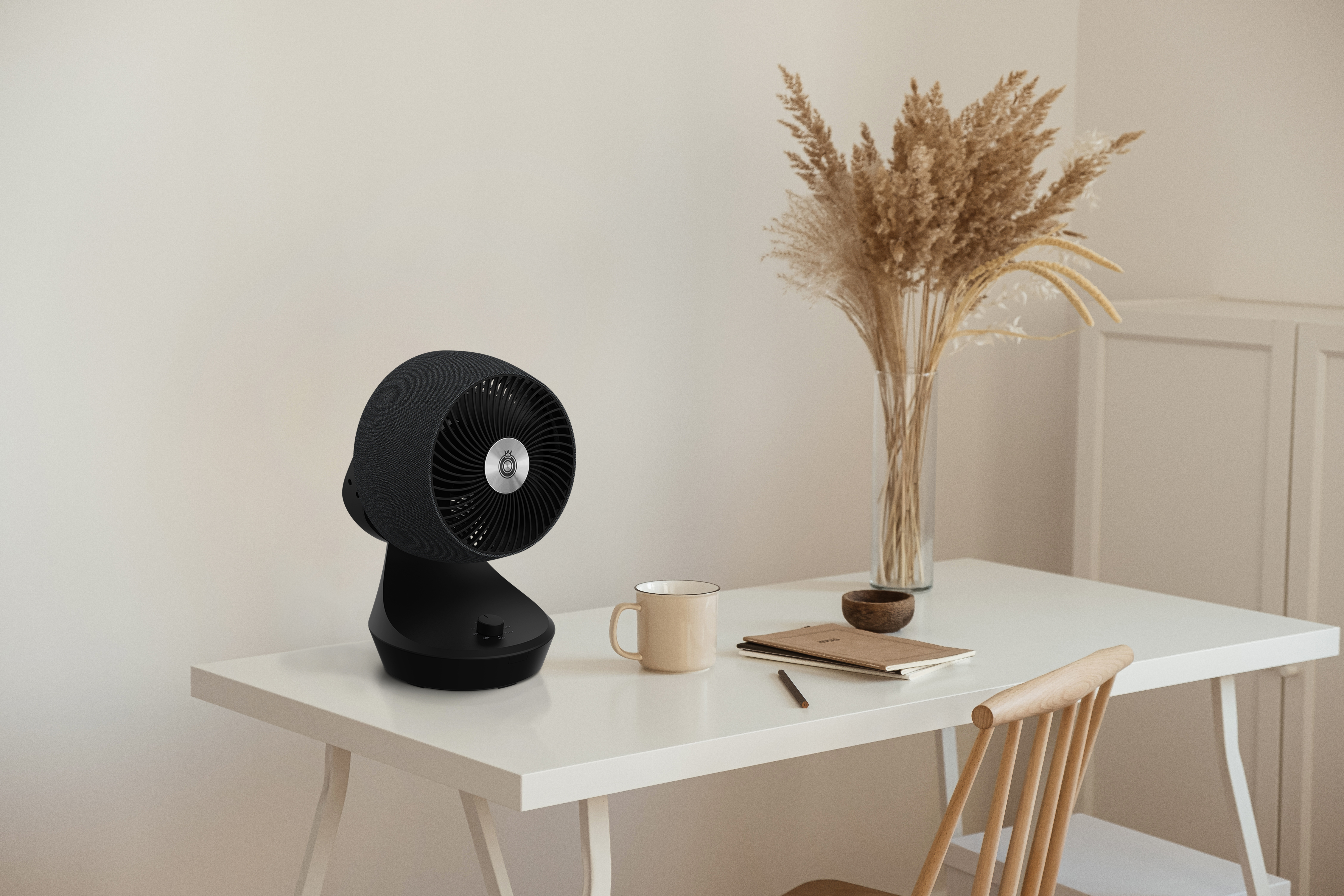 Ein schwarzer Tischventilator steht auf einem weißen Schreibtisch neben einer Tasse und Büchern.
