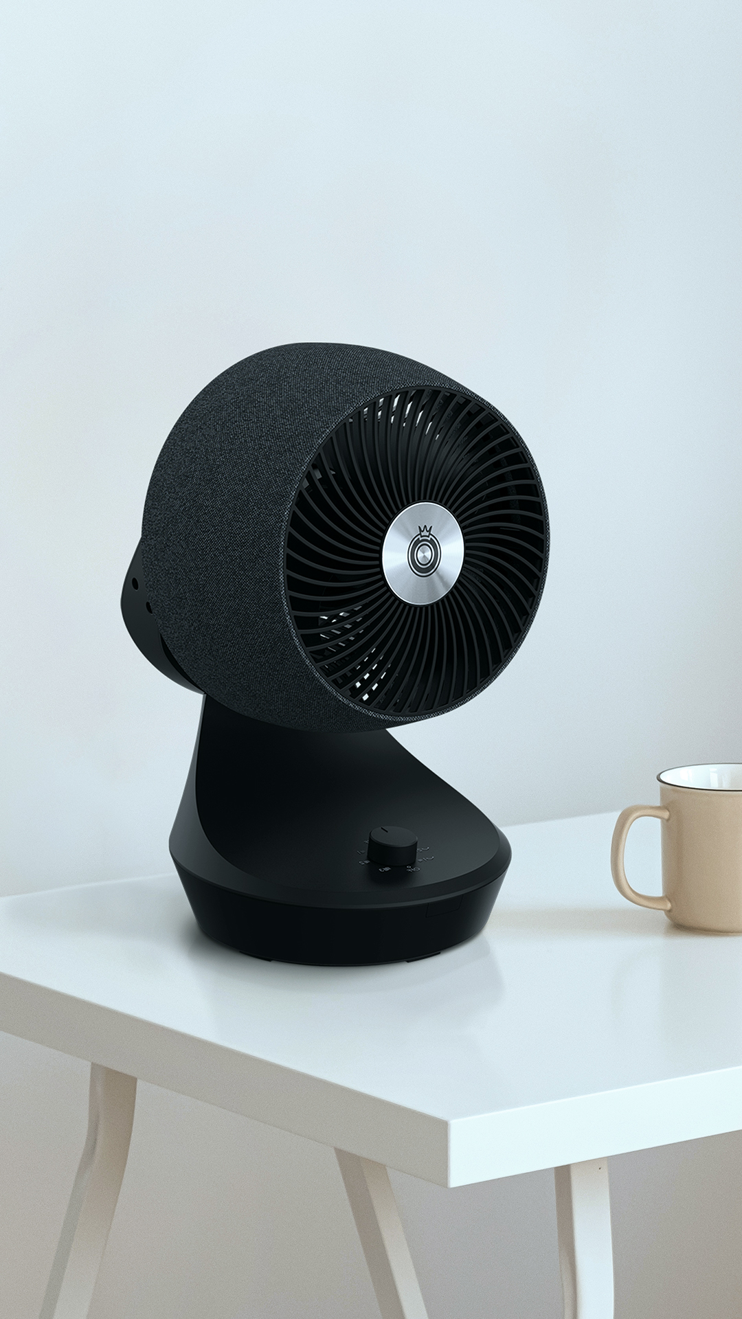 Ein schwarzer Ventilator mit Stoffbezug steht neben einer beigefarbenen Tasse auf einem weißen Tisch.