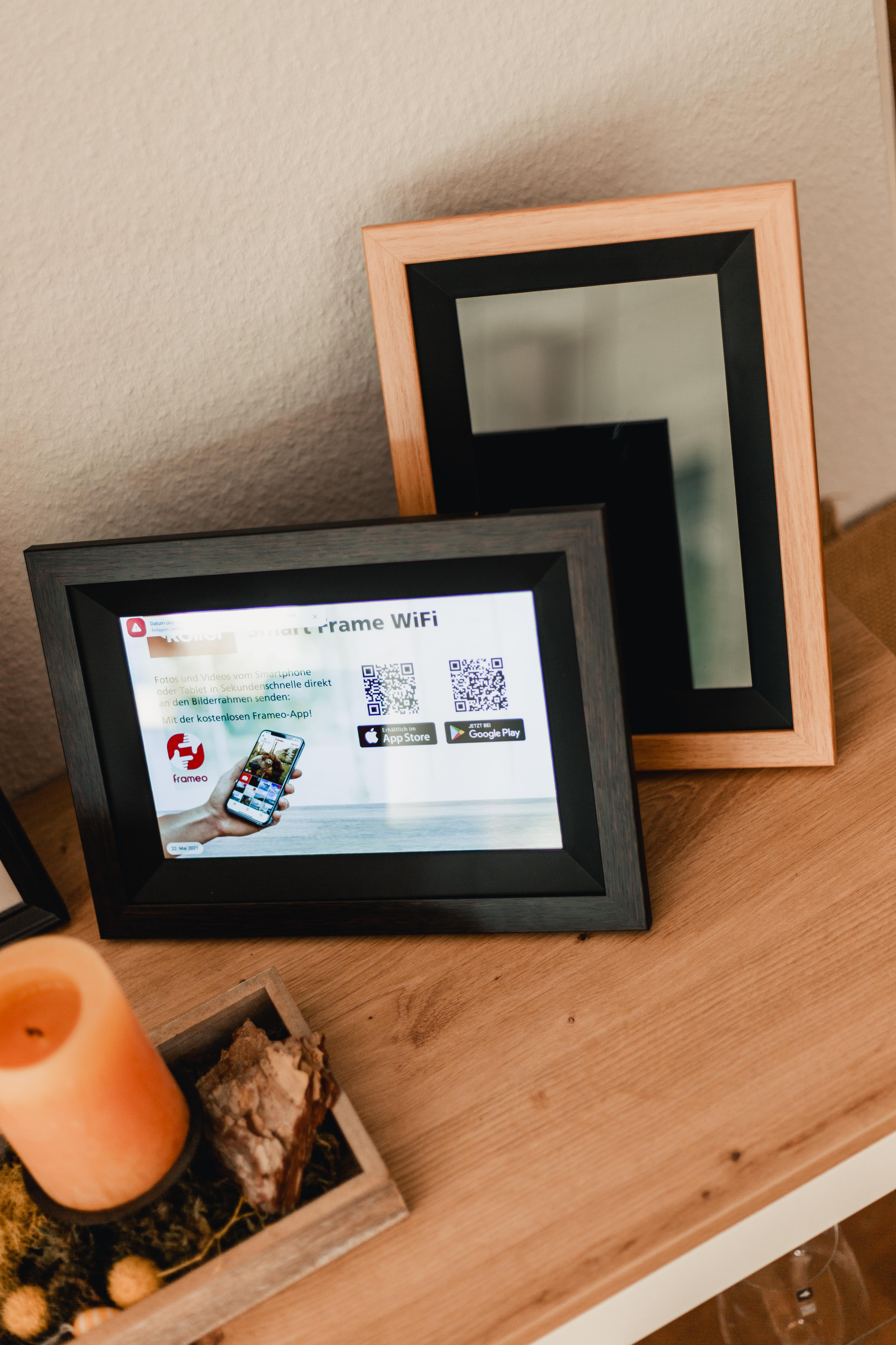 Ein digitaler Bilderrahmen zeigt die Frameo-App mit QR-Codes. Daneben ein Kerzenhalter.