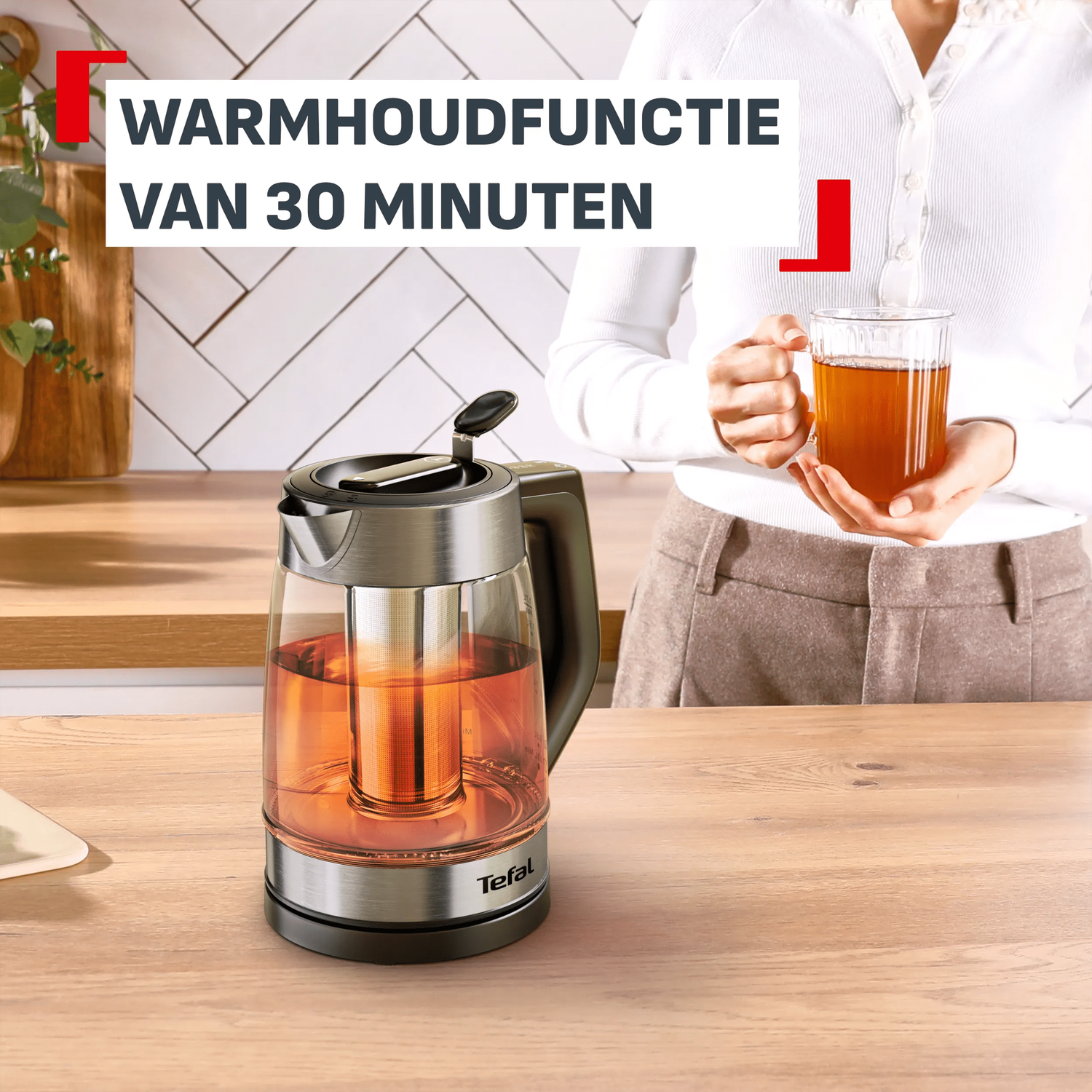 Glazen theepot met warme thee en een persoon die een kop vasthoudt.