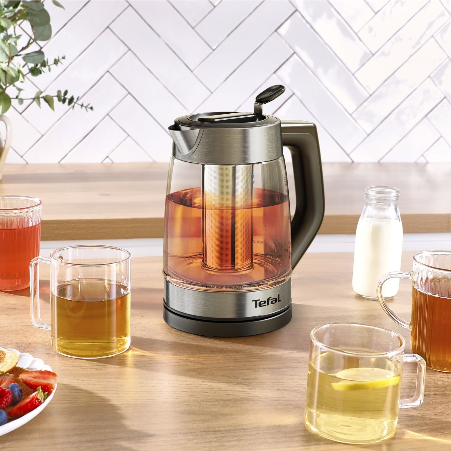 Glazen waterkoker met thee, ernaast glazen thee en een bord fruit.
