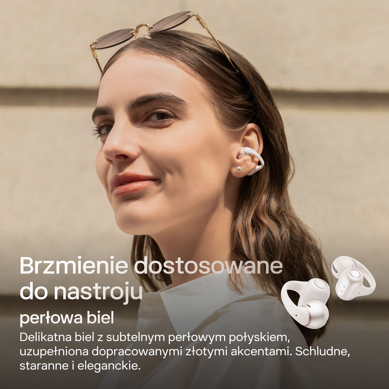 Kobieta nosi białe słuchawki, okulary przeciwsłoneczne na głowie. Dwa kolejne słuchawki leżą obok.