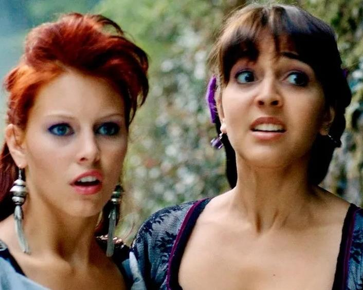 Zwei Frauen mit ausdrucksstarken Gesichtern im Freien, eine mit roten Haaren, die andere mit dunklen Haaren.