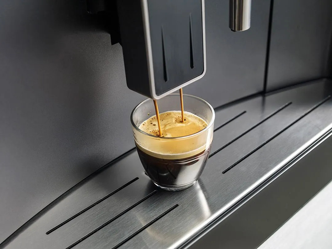 Espresso nalewane do szklanki z ekspresu do kawy, zbliżenie.