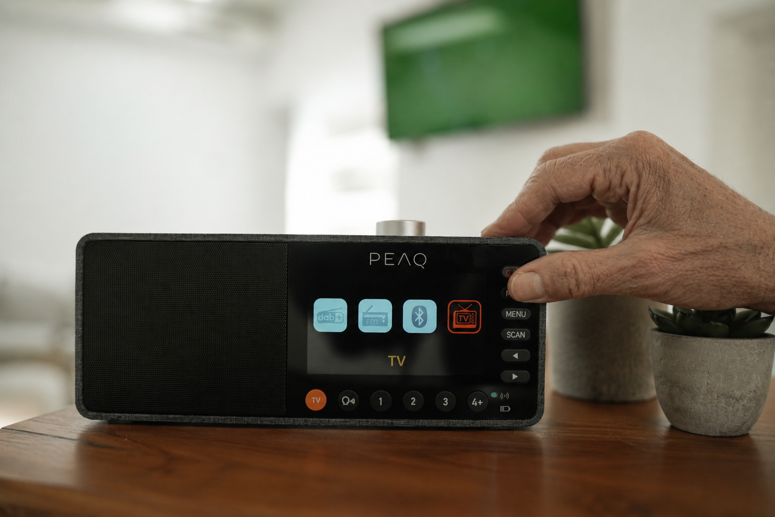 Eine Hand bedient ein PEAQ Radio mit Touchscreen und verschiedenen Symbolen.