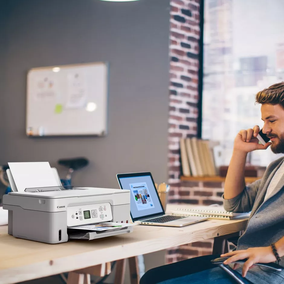 Ein Mann telefoniert neben einem Drucker und Laptop in einem modernen Büro.