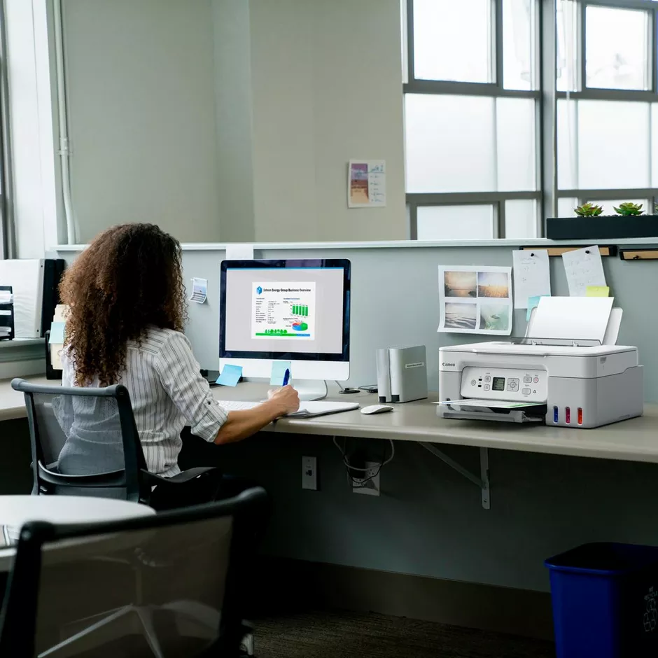 Frau am Schreibtisch mit Computer und Drucker im Büro.