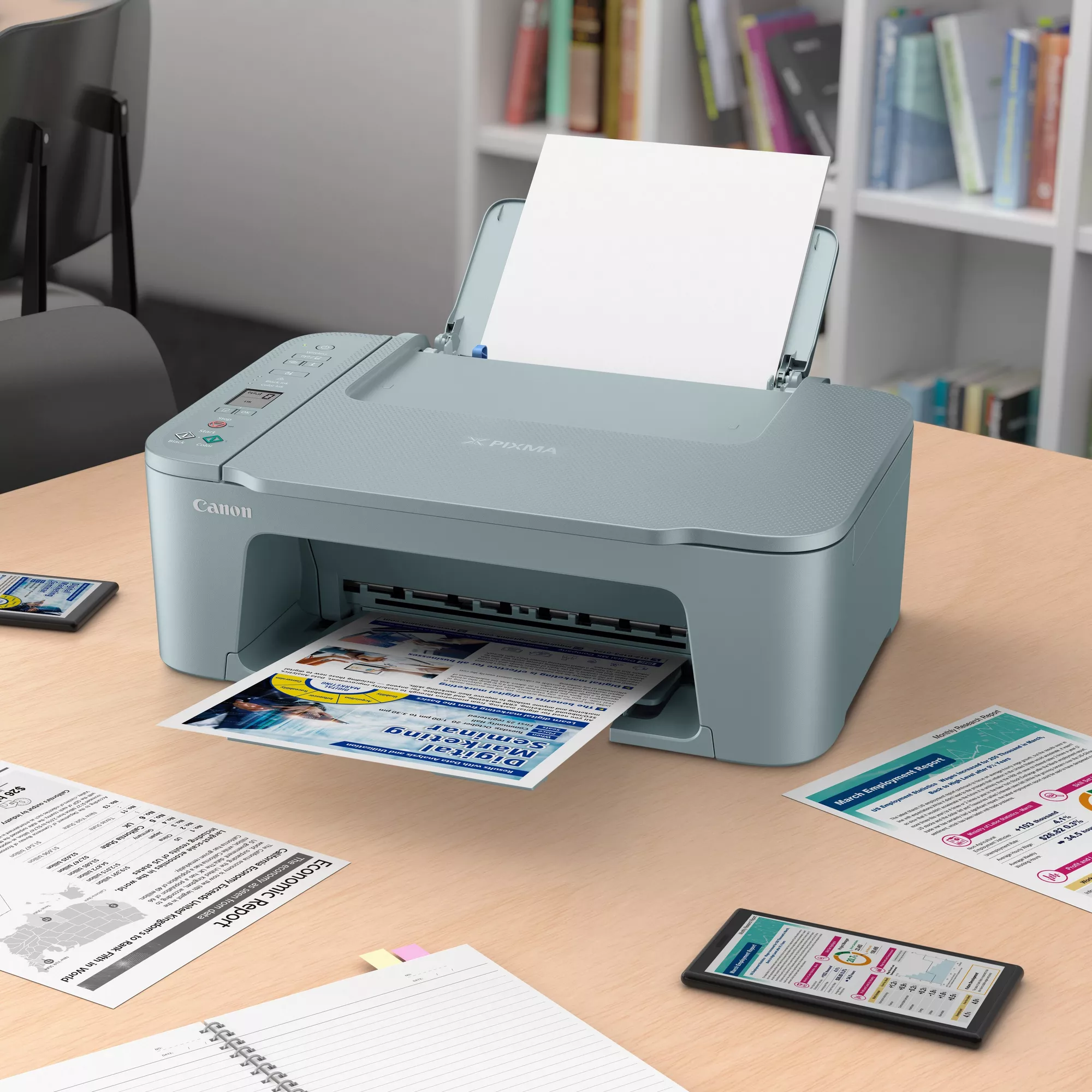 Ein grauer Canon Pixma Drucker druckt ein Blatt auf einem Holztisch mit Büchern im Hintergrund.